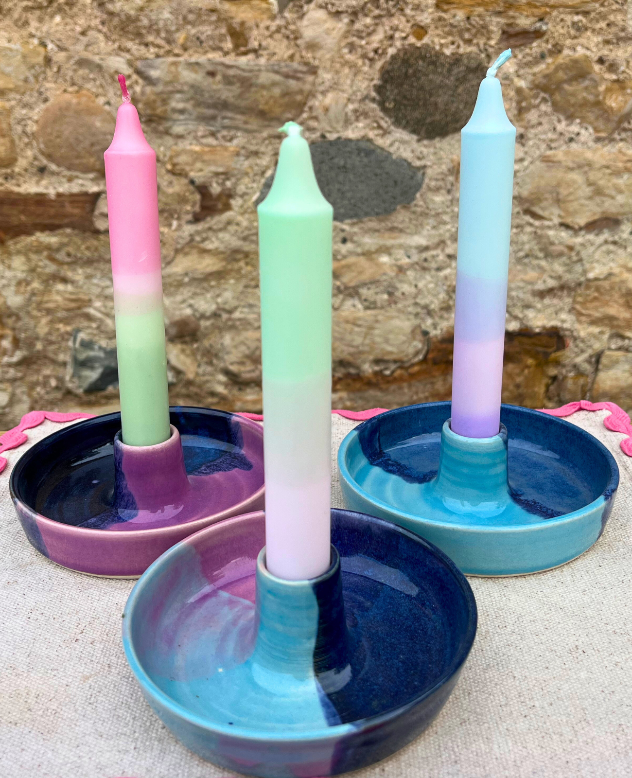 Three ceramic candle holders with colorful candles against a stone wall background