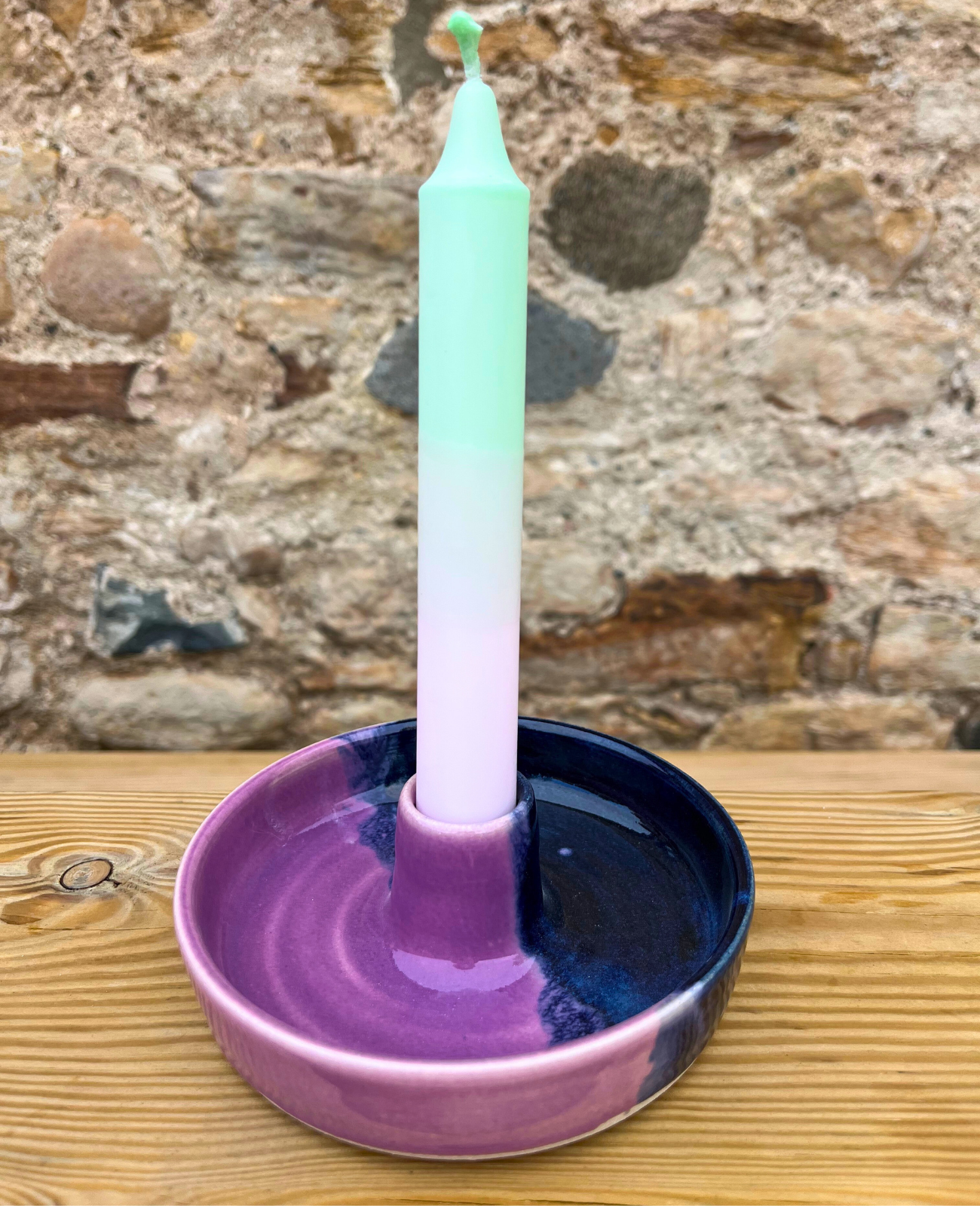Candle in a purple holder on a wooden surface with a stone wall background