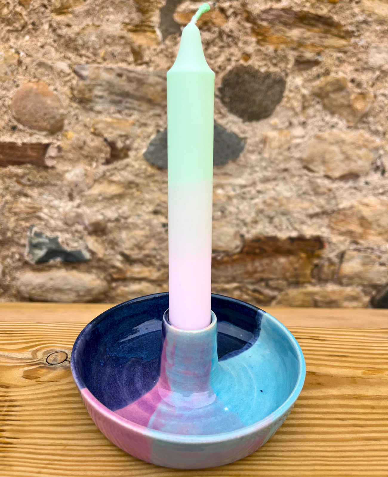 Ceramic candle holder with a gradient candle against a stone wall background