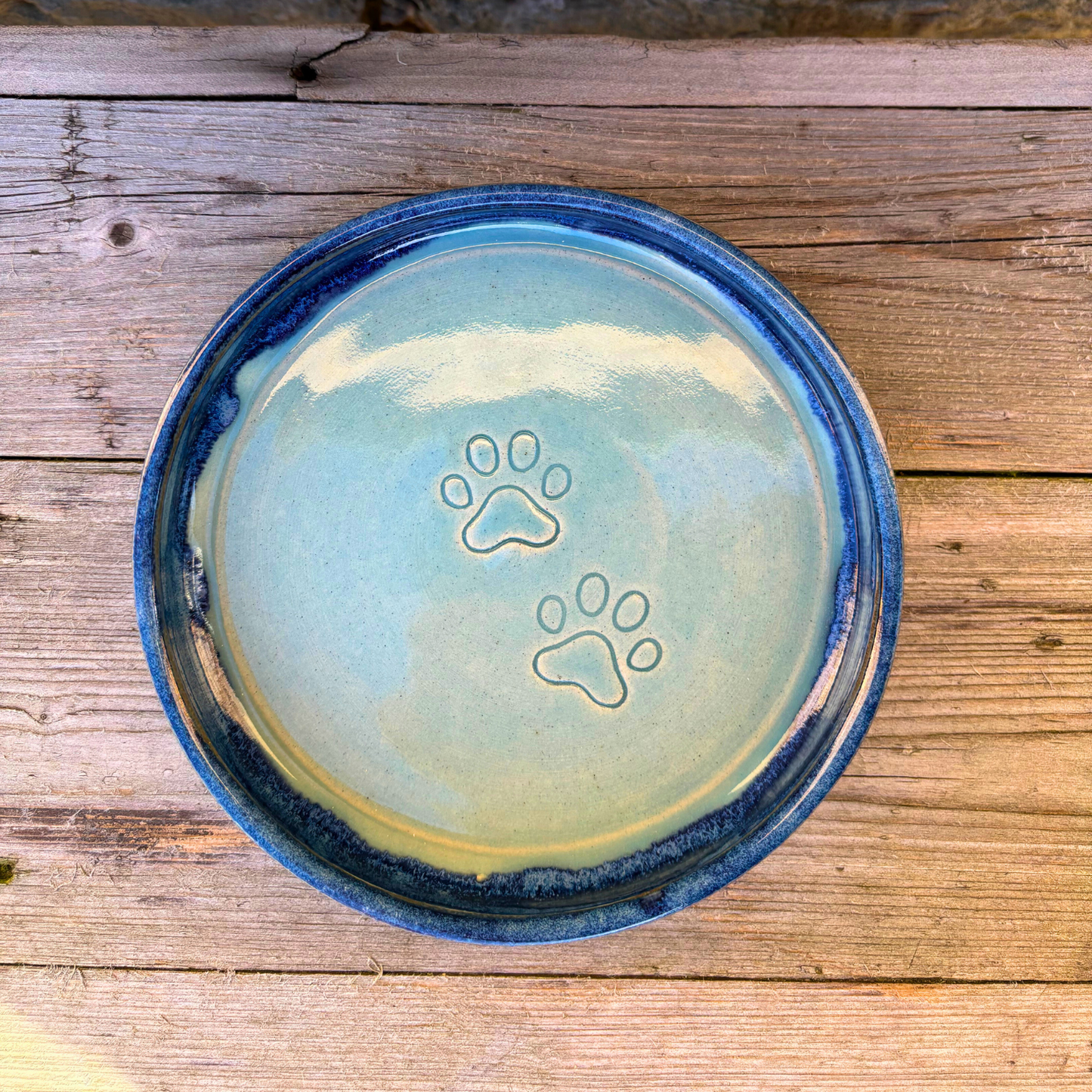 Ceramic pet bowl with paw prints on a wooden surface