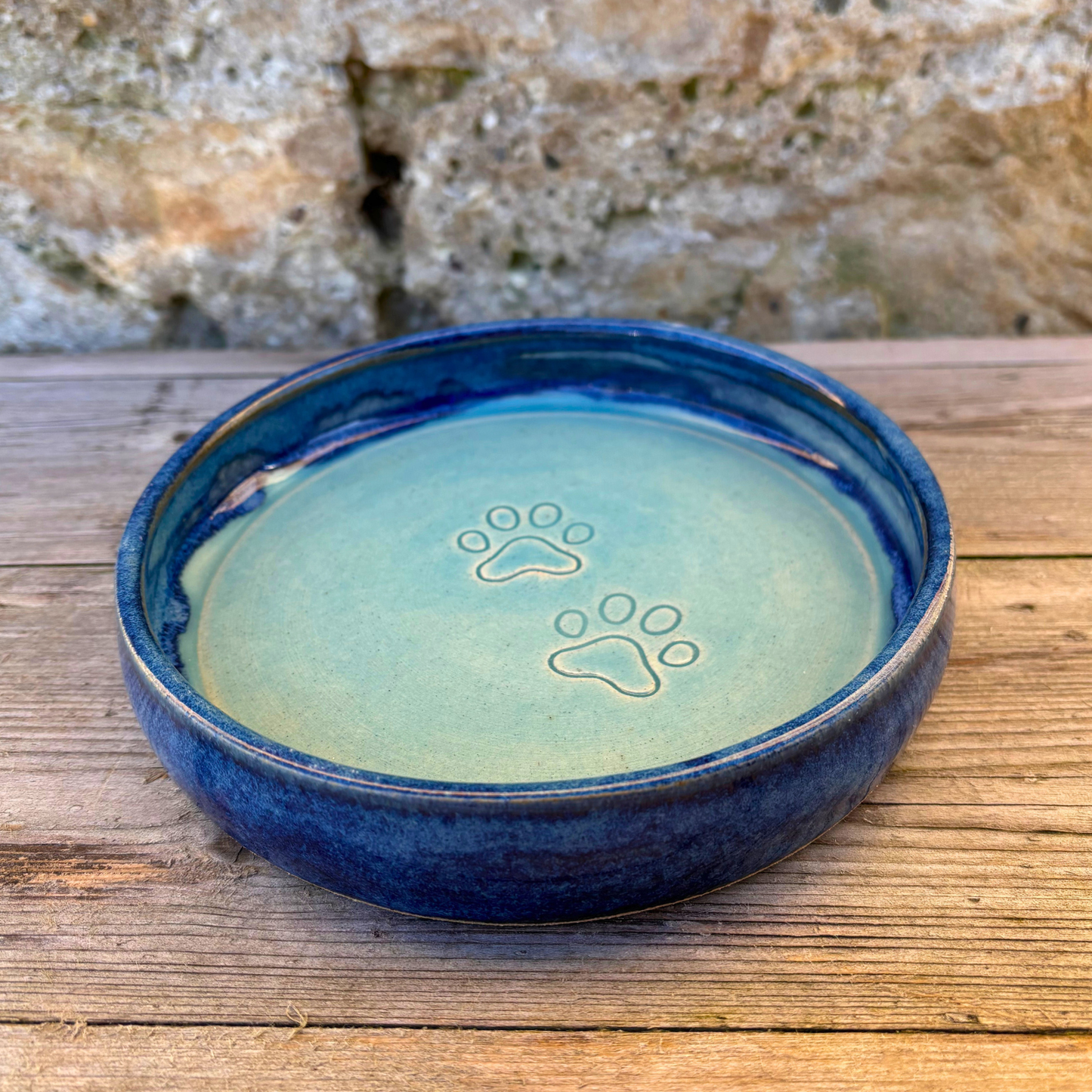 Blue ceramic bowl with paw prints on a wooden surface