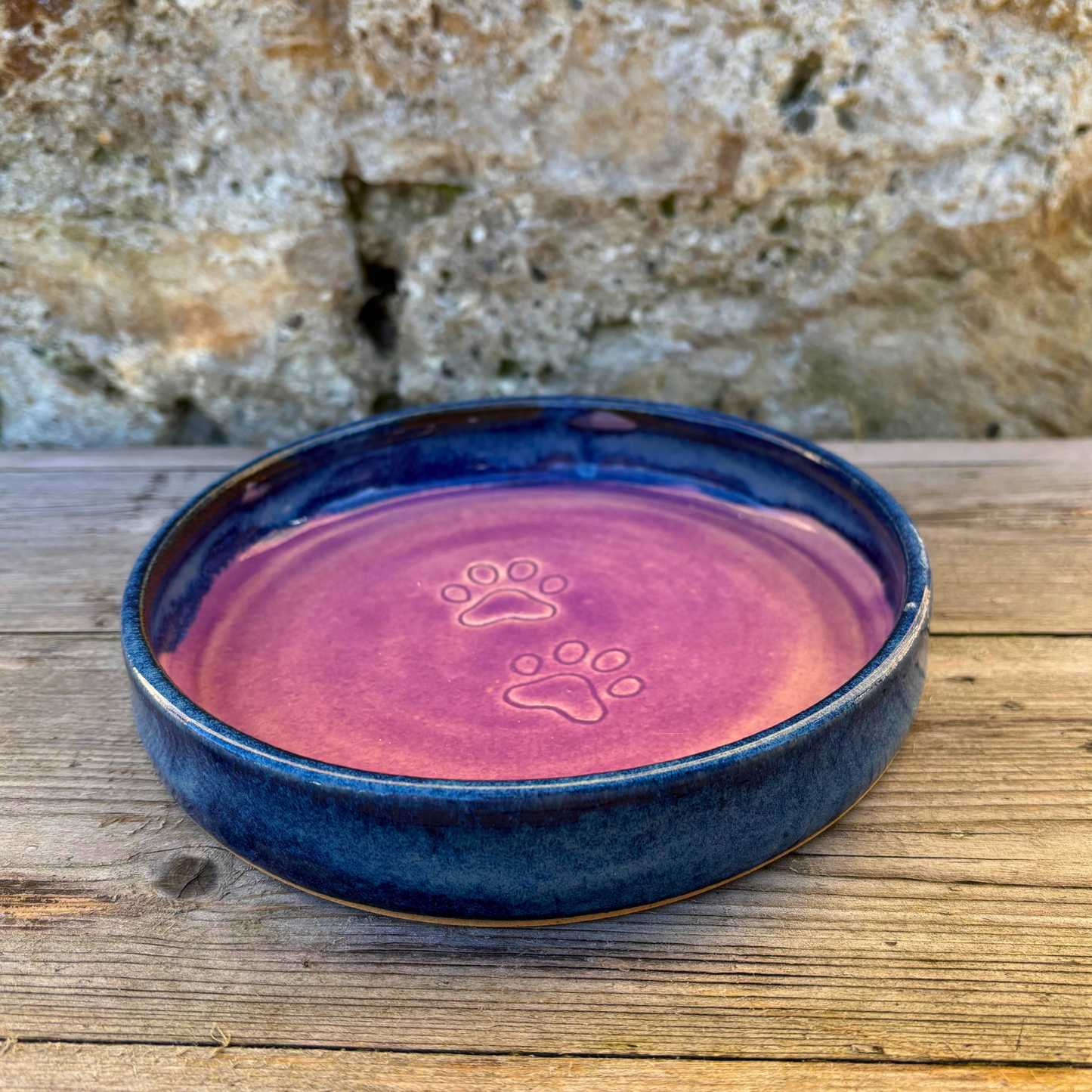 Ceramic pet bowl with paw prints on a wooden surface and stone background