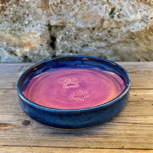 Ceramic pet bowl with paw prints on a wooden surface and stone background