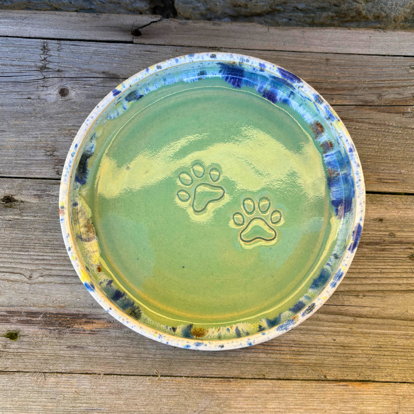 Green ceramic dish with paw prints on a wooden surface