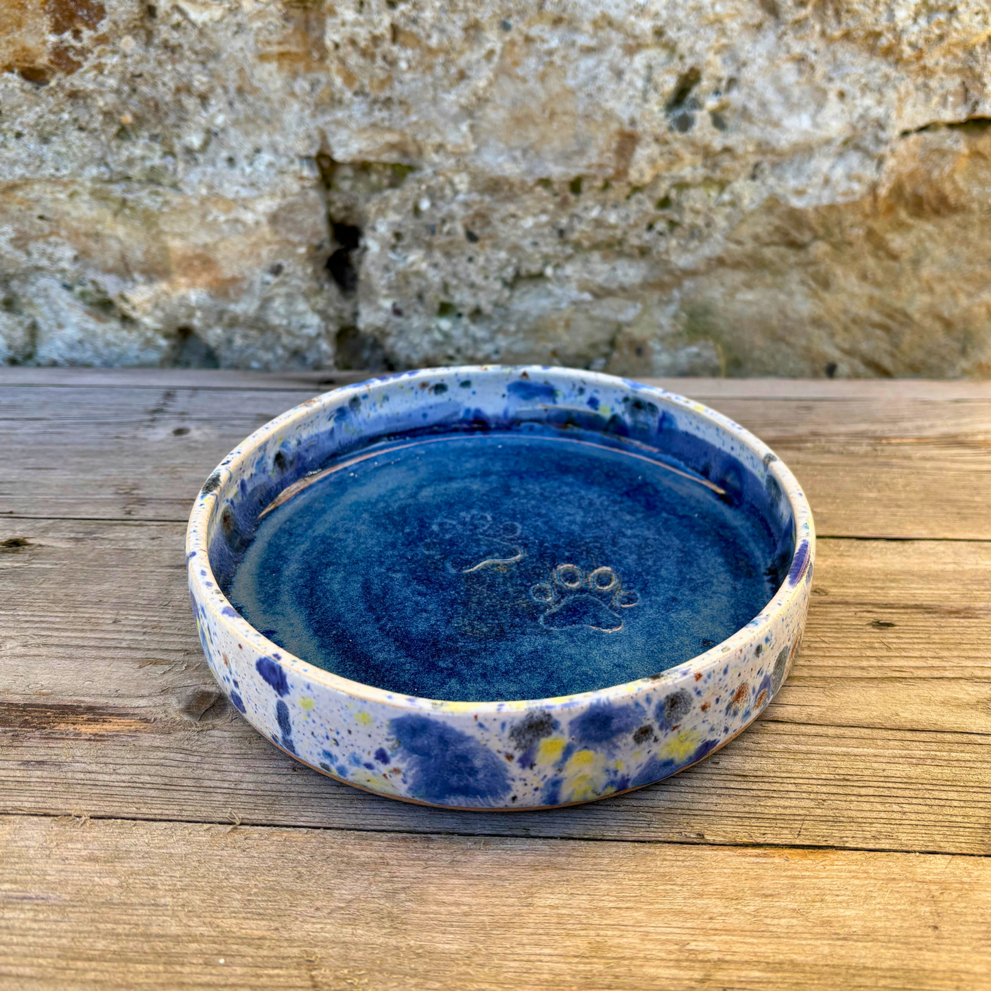 Blue ceramic bowl with speckled design on a wooden surface with a stone wall background