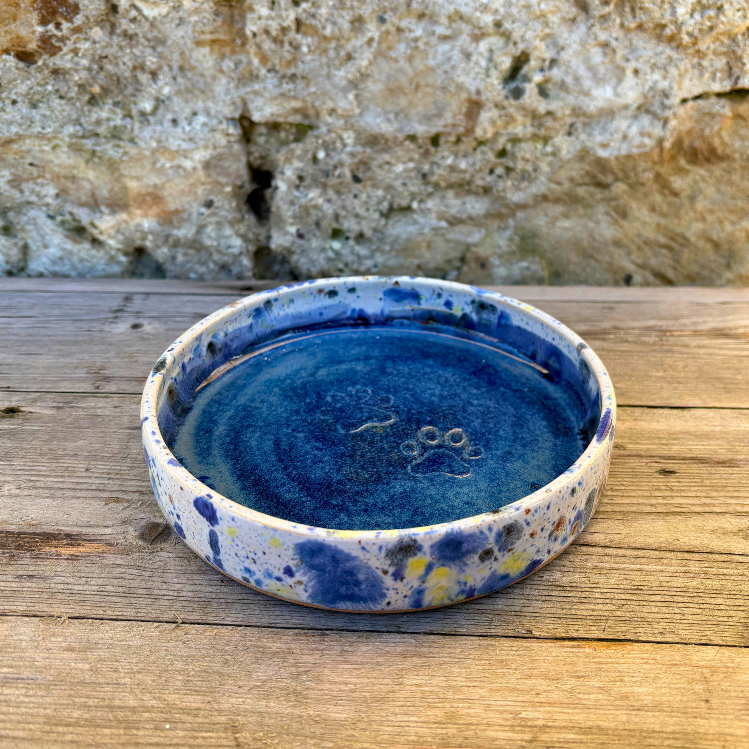 Blue ceramic bowl with speckled design on a wooden surface with a stone wall background