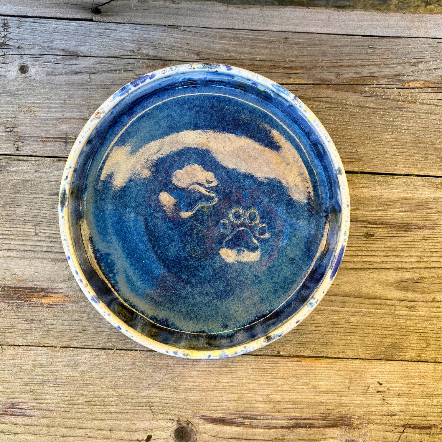 Ceramic plate with blue glaze and paw print design on a wooden surface