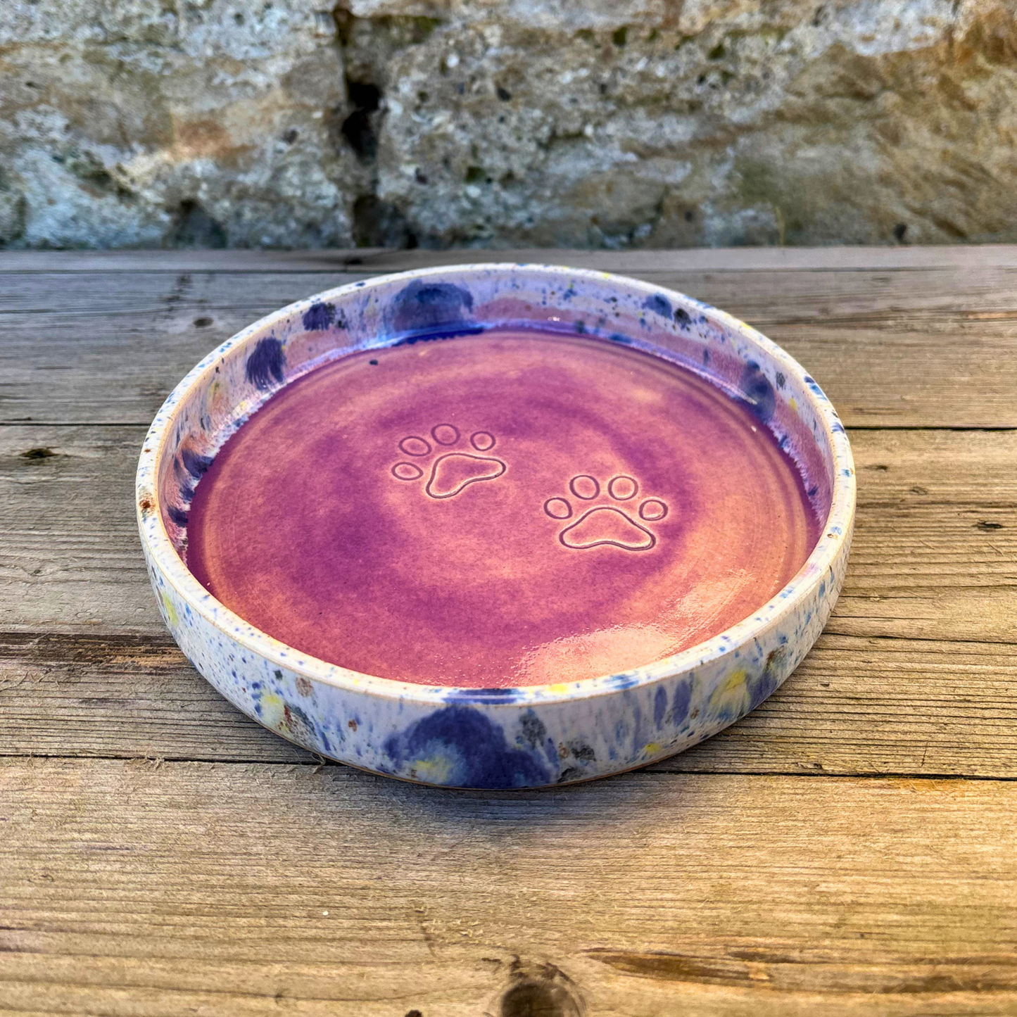 Ceramic pet bowl with paw prints on a wooden surface