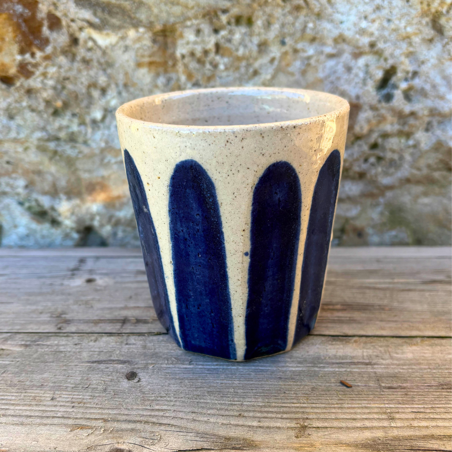 Ceramic cup with blue decorative stripes on a wooden surface with a stone wall background
