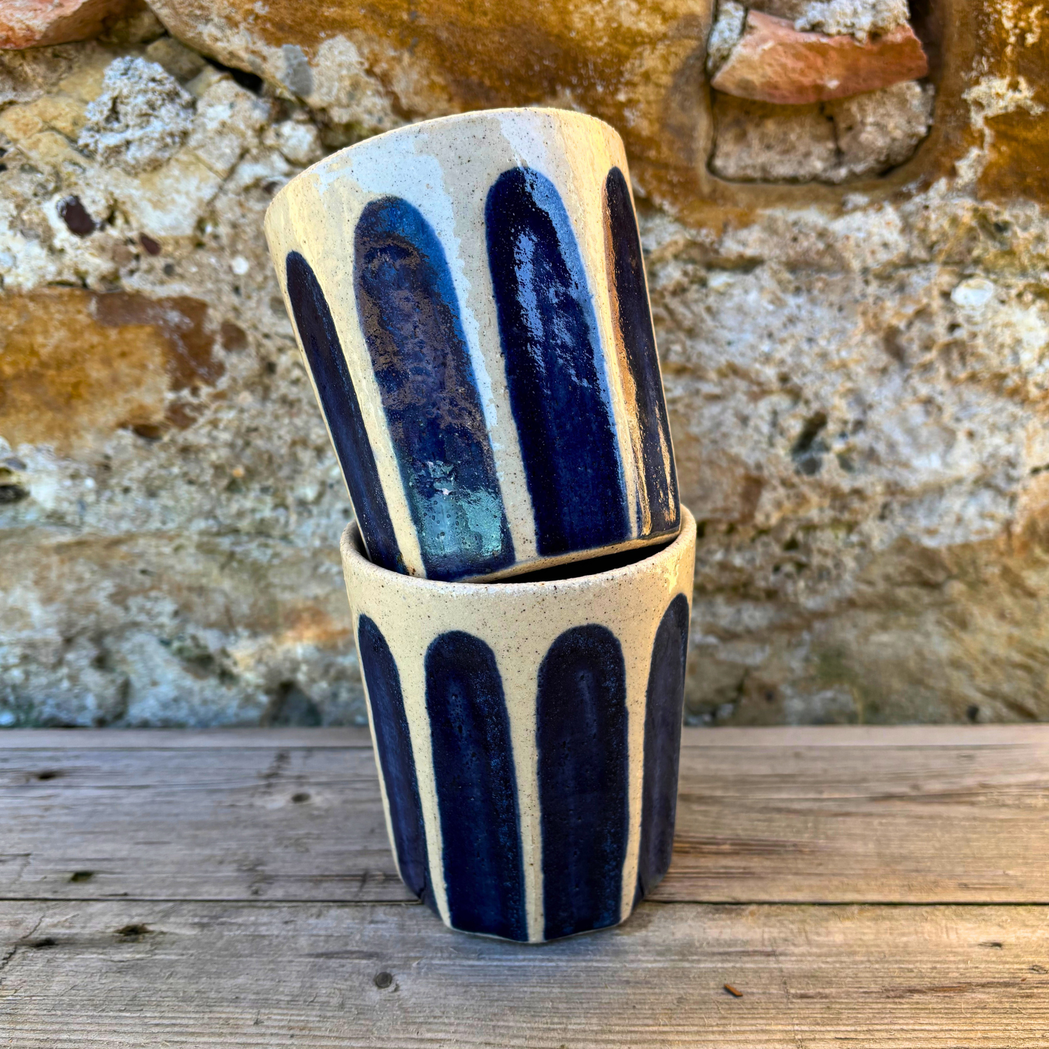 Ceramic cup with blue stripes on a wooden surface against a stone wall background
