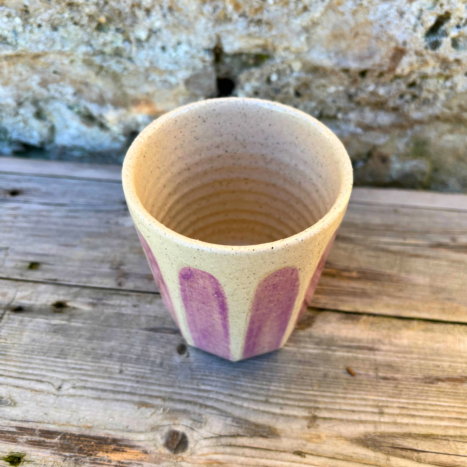 Ceramic cup with pink design on a wooden surface with a stone background
