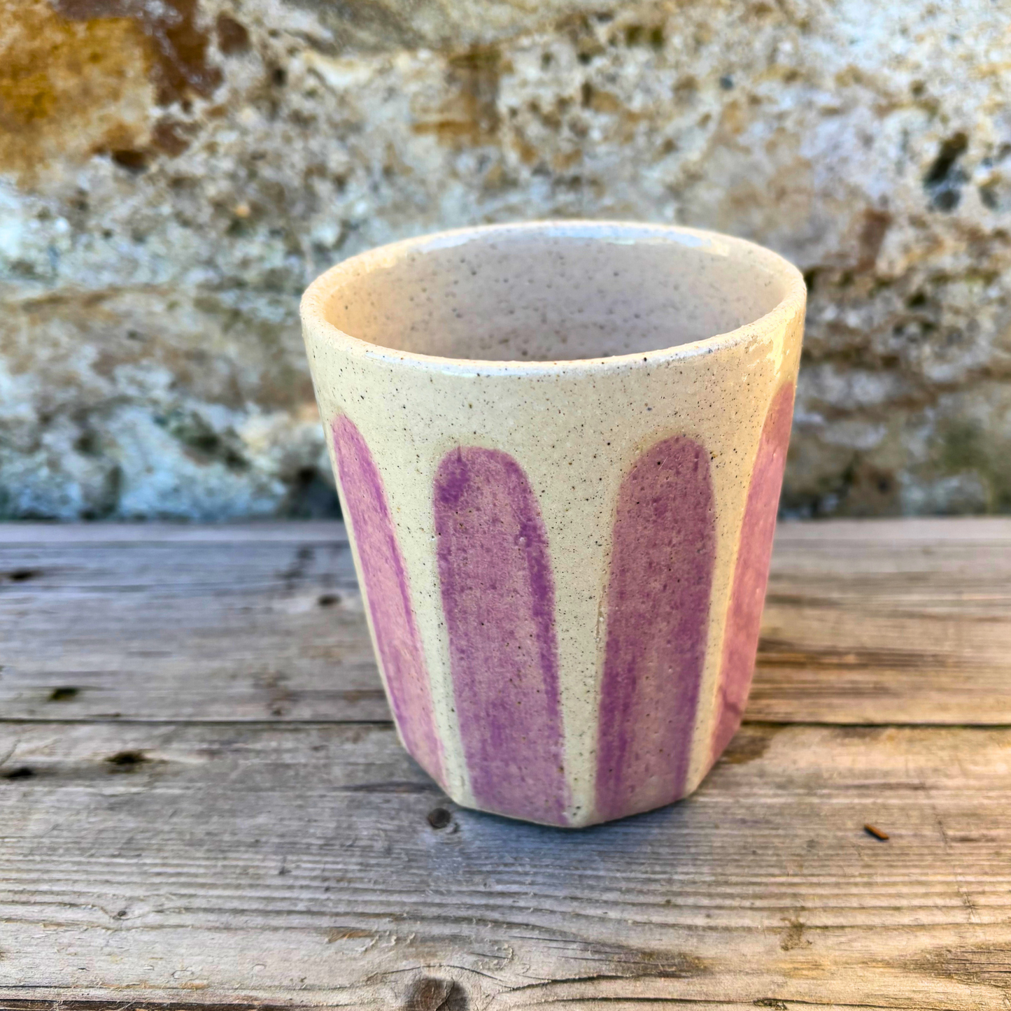 Ceramic cup with pink stripes on a wooden surface with a stone background