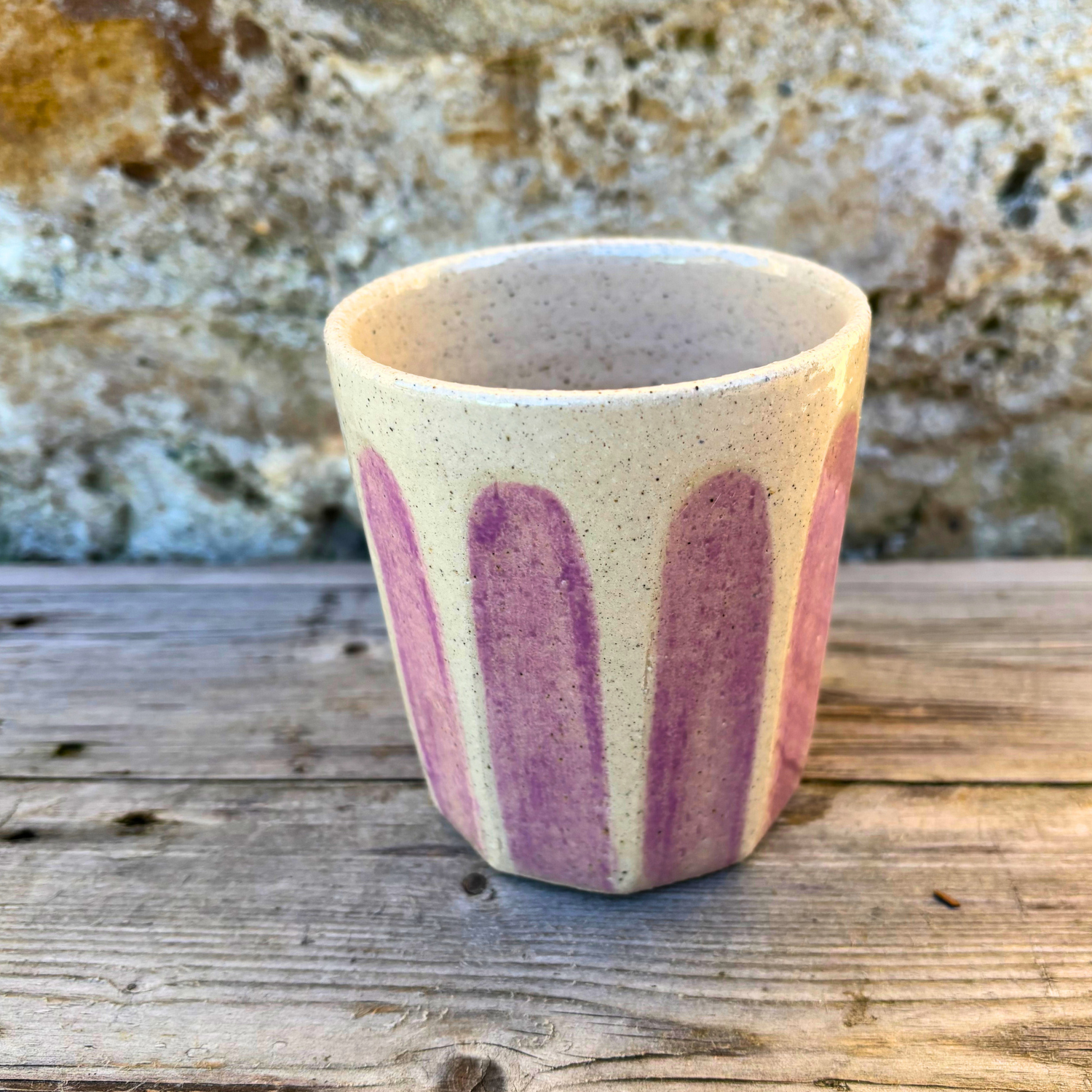 Ceramic cup with pink stripes on a wooden surface with a stone background