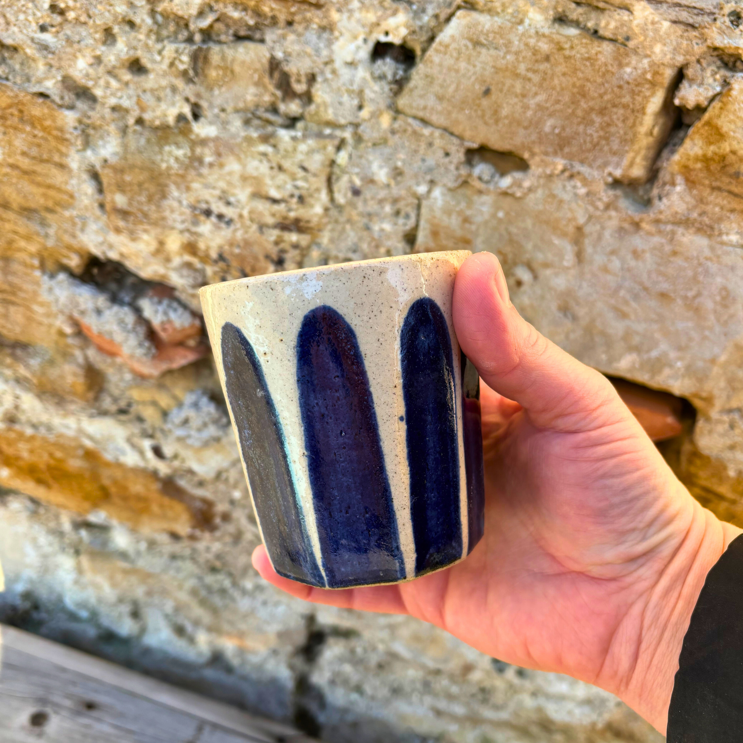 Hand holding a ceramic mug with blue stripes against a stone wall background
