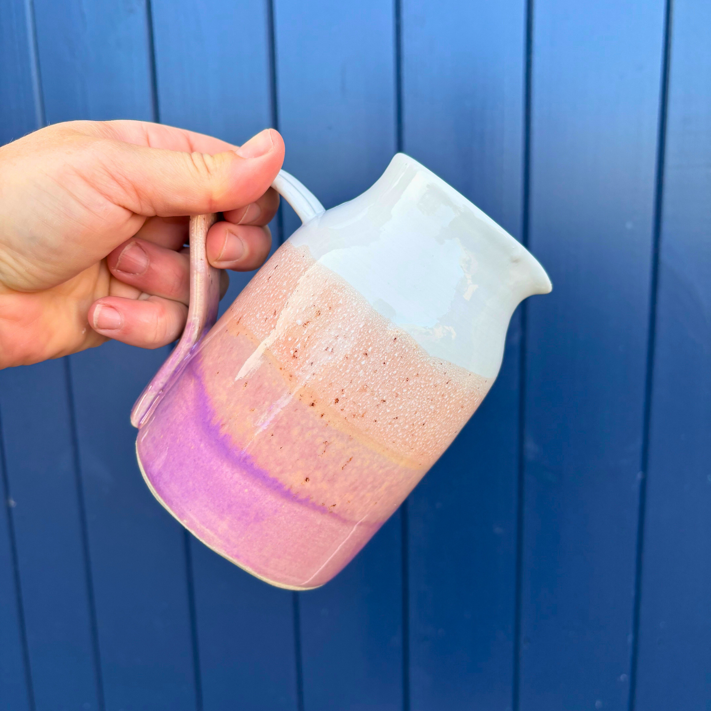 Hand holding a ceramic jug with a gradient design against a blue background
