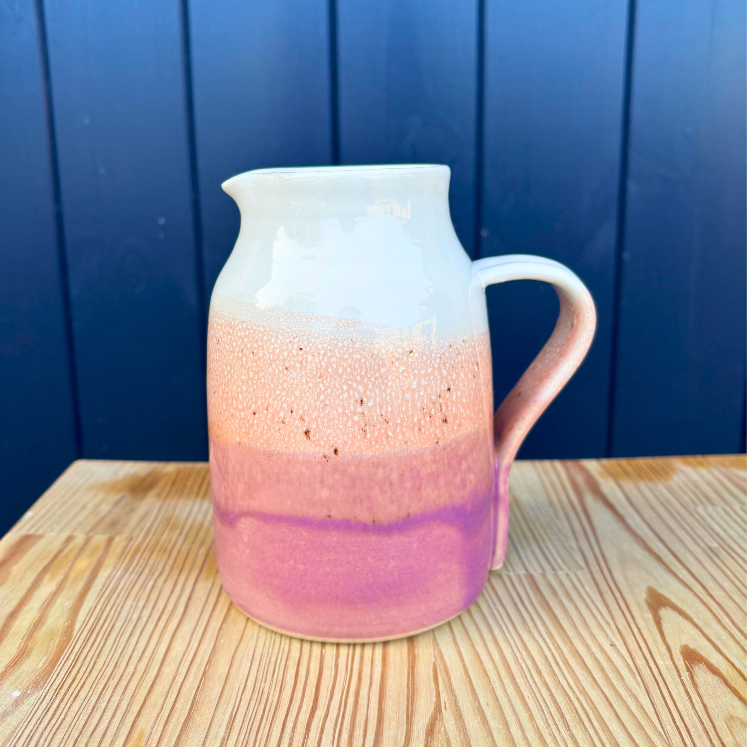 Ceramic pitcher with gradient design on a wooden surface against a blue wall