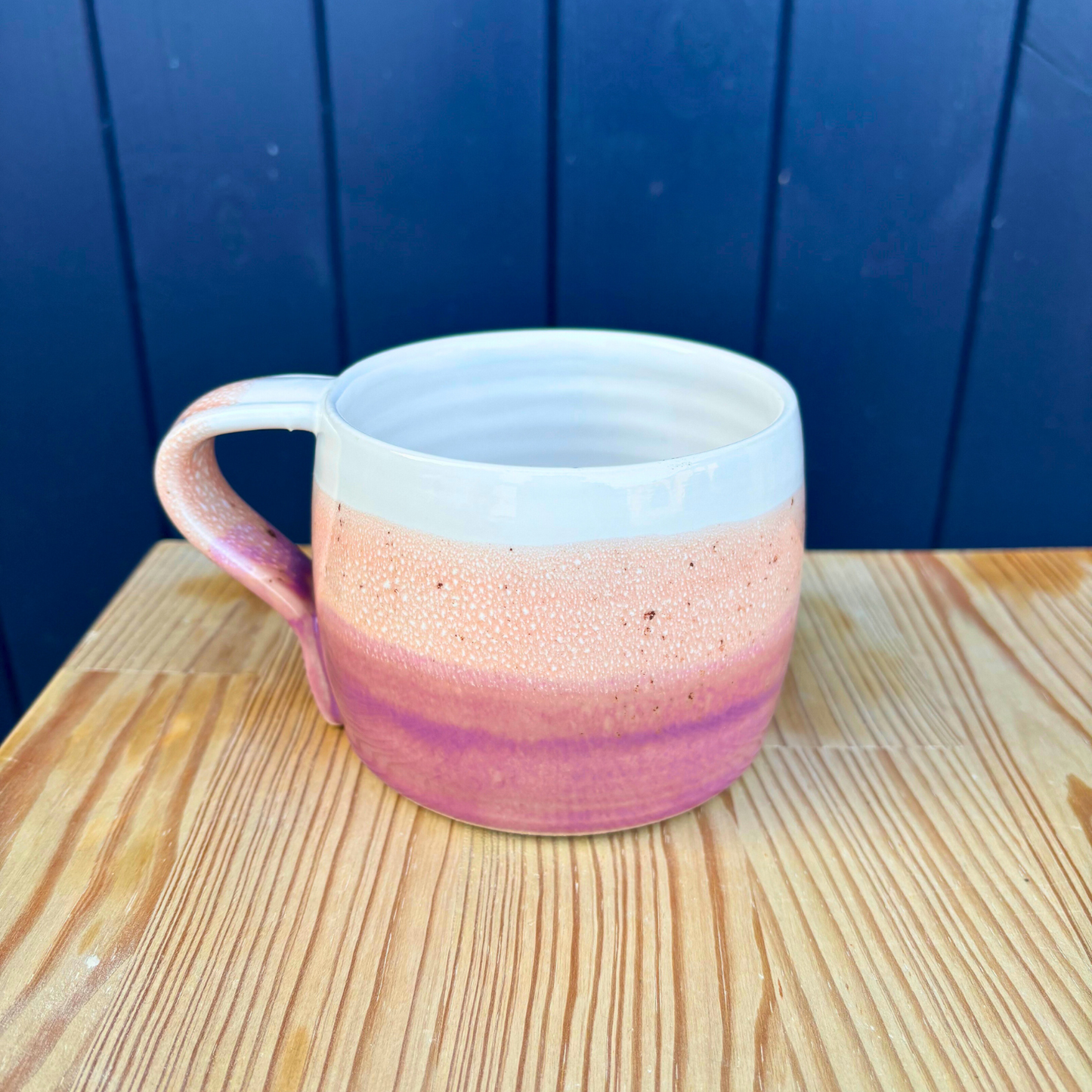 Ceramic mug with gradient pink to white design on a wooden surface with blue background