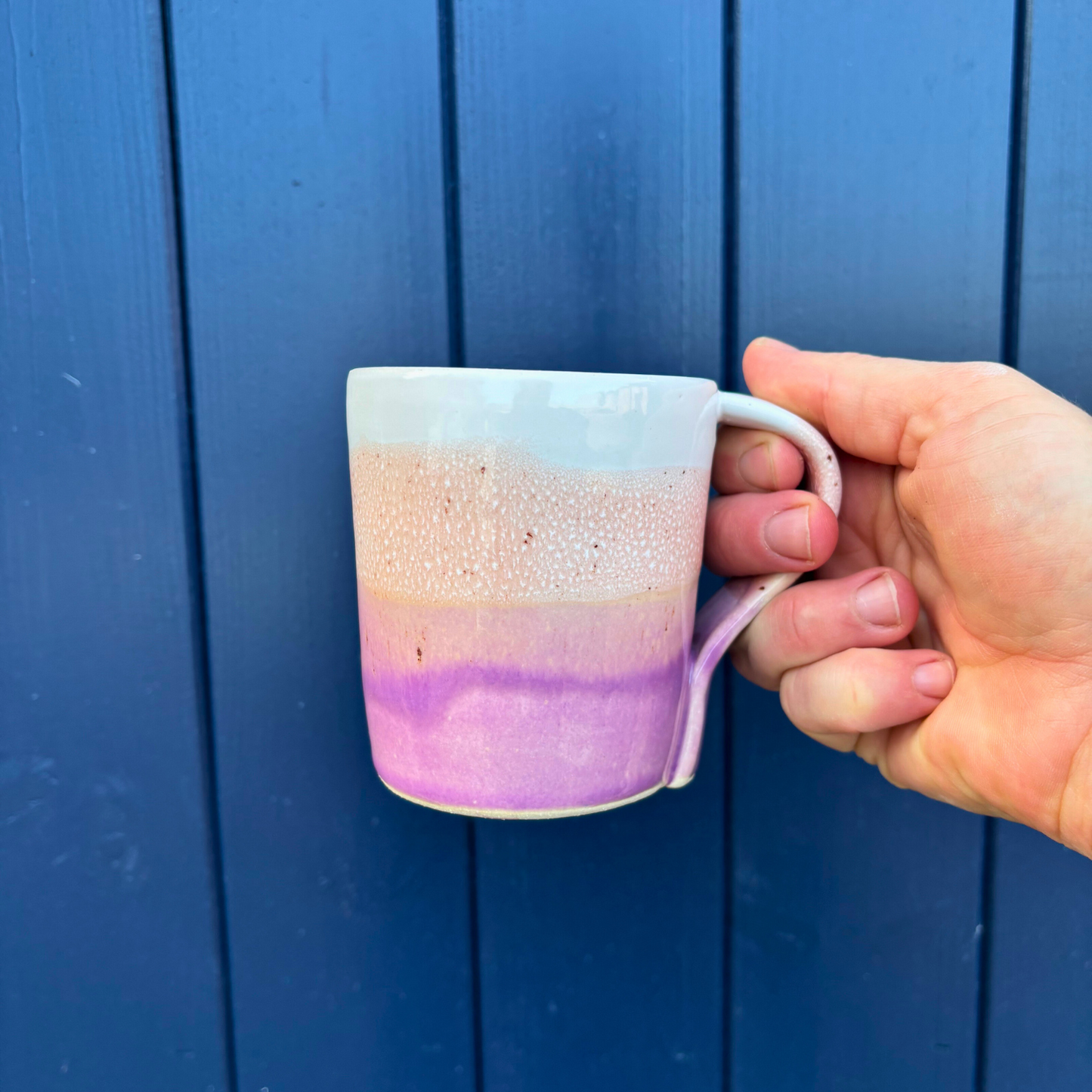 Hand holding a ceramic mug with a gradient design against a blue wooden background
