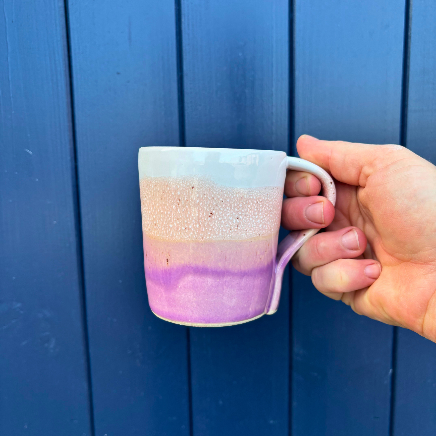 Hand holding a ceramic mug with a gradient design against a blue wooden background