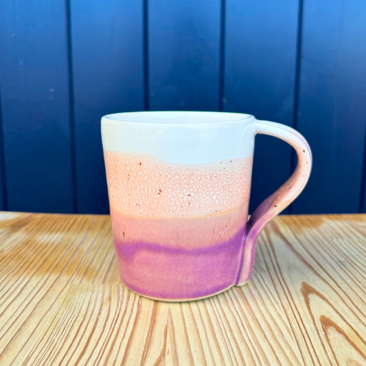 Ceramic mug with gradient design on a wooden surface against a blue wall
