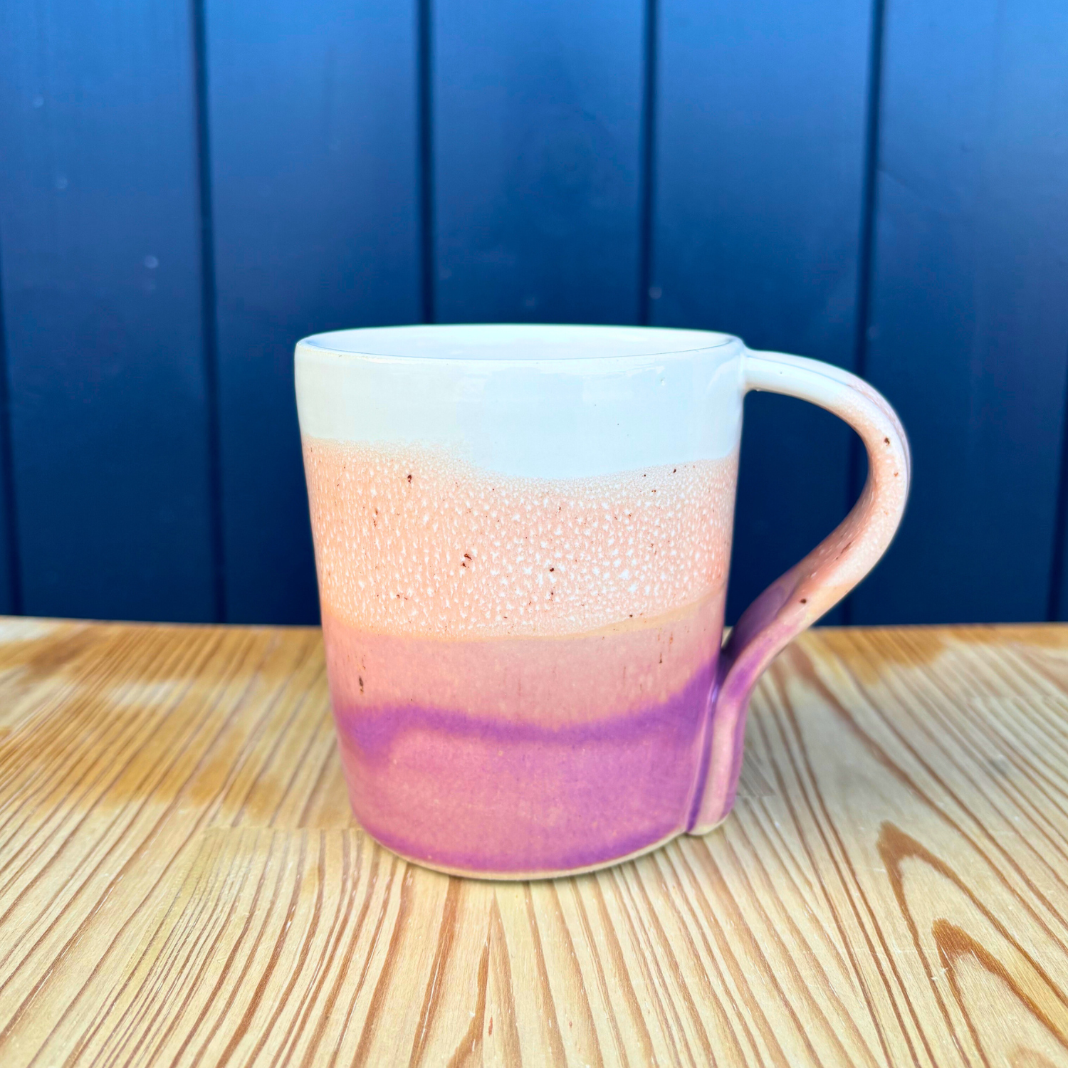 Ceramic mug with gradient design on a wooden surface against a blue wall