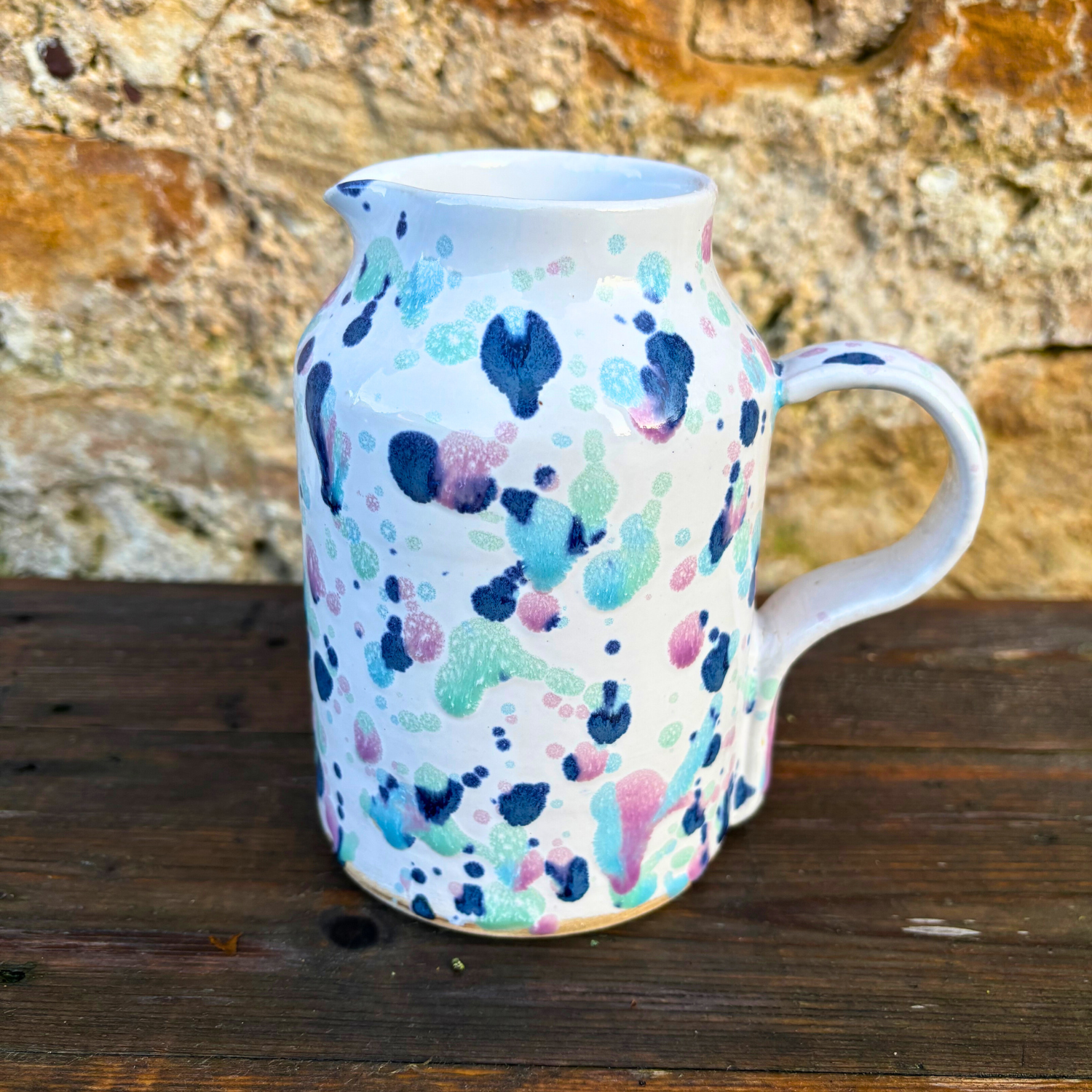 Ceramic pitcher with colorful abstract pattern on a wooden surface