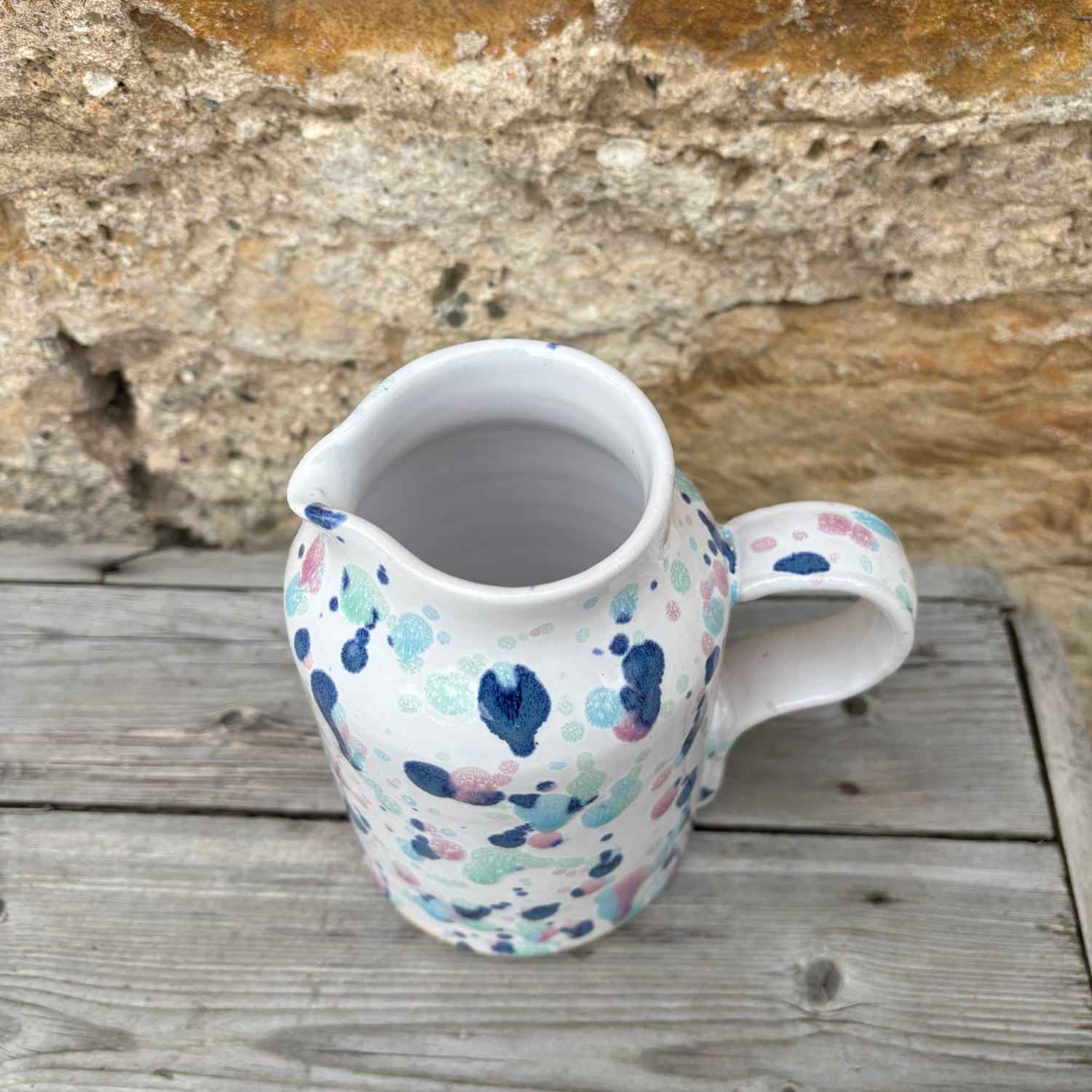 Ceramic pitcher with colorful abstract pattern on a wooden surface with stone wall background