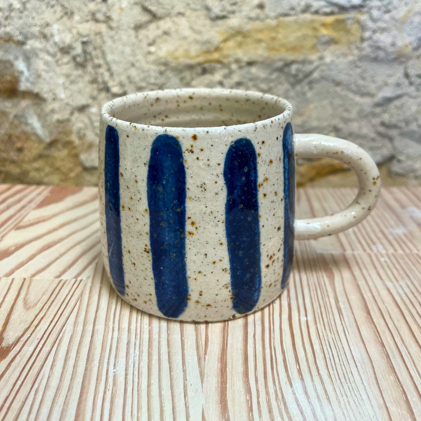Ceramic mug with blue stripes on a wooden surface with a stone wall background