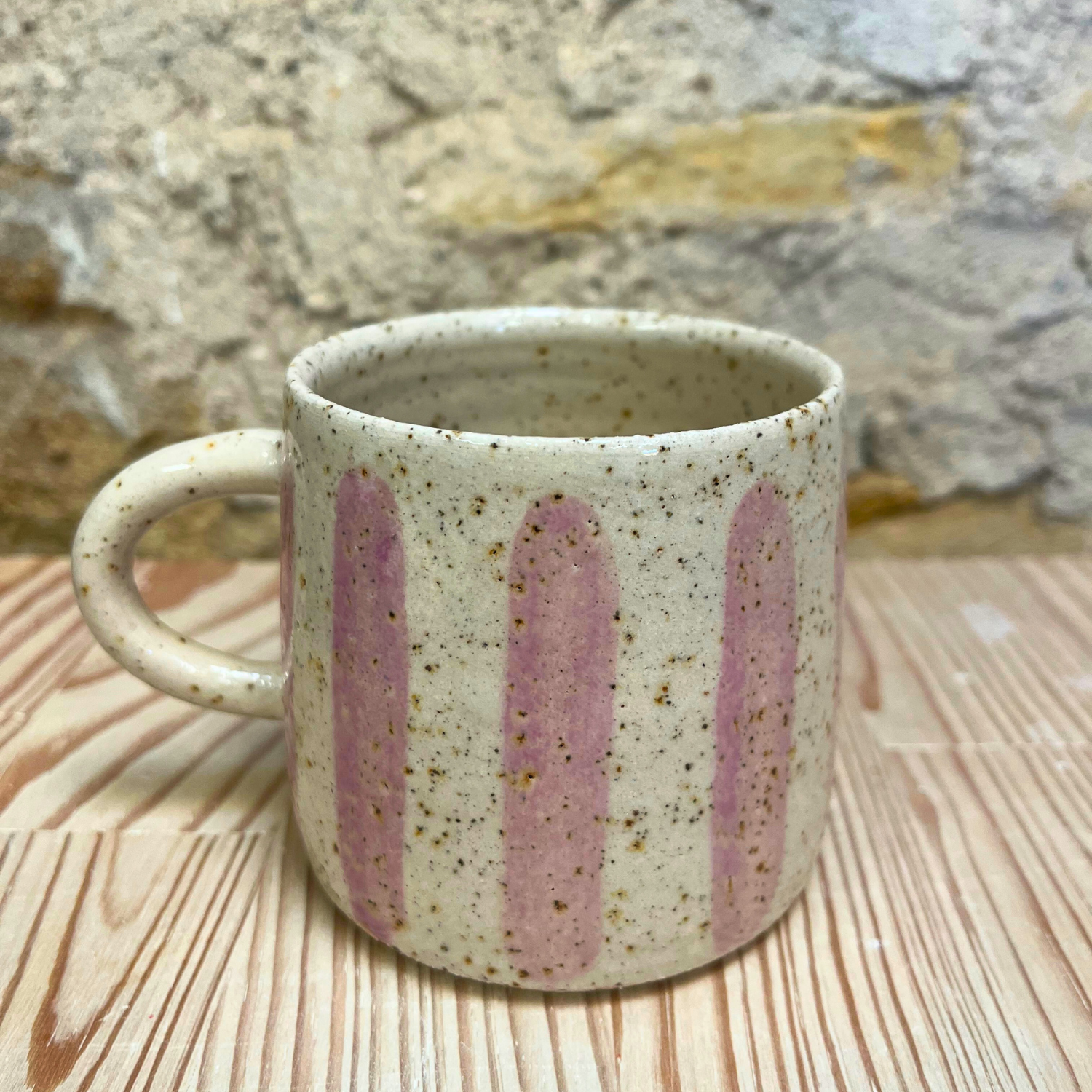Speckled ceramic mug with pink stripes on a wooden surface with stone background