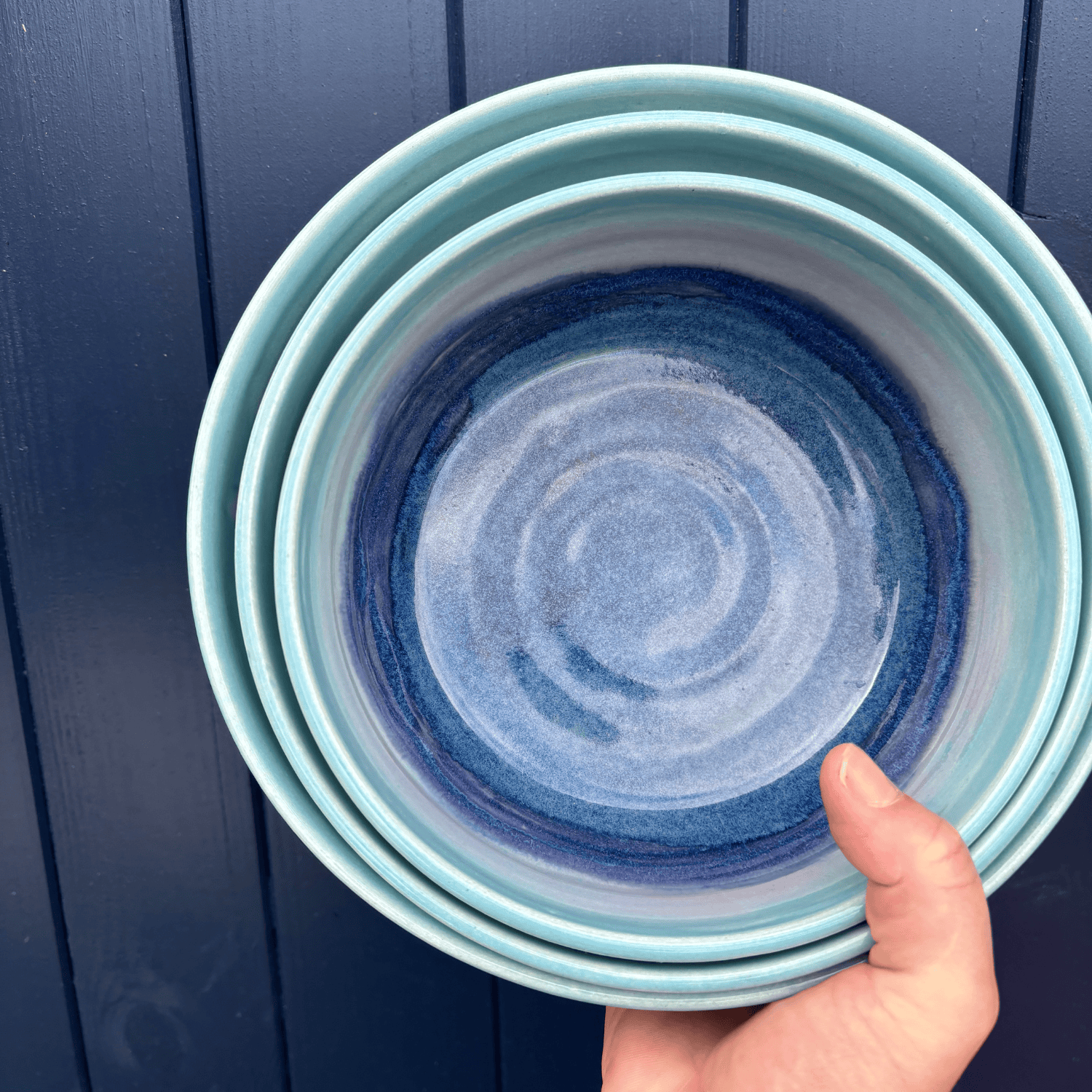 Stack of blue ceramic bowls held against a dark blue wooden background