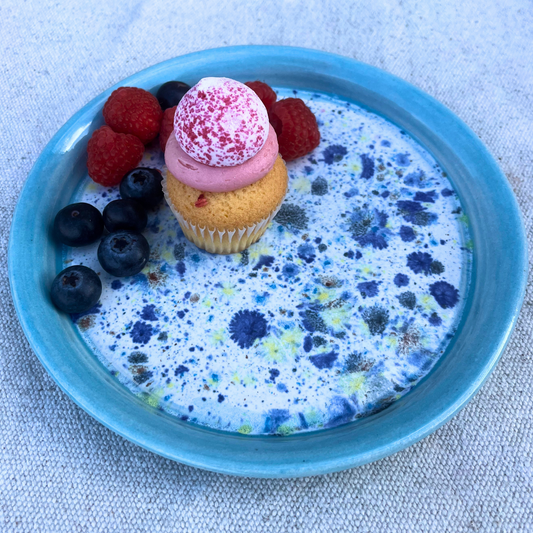 Cupcake with pink frosting and berries on a blue speckled plate