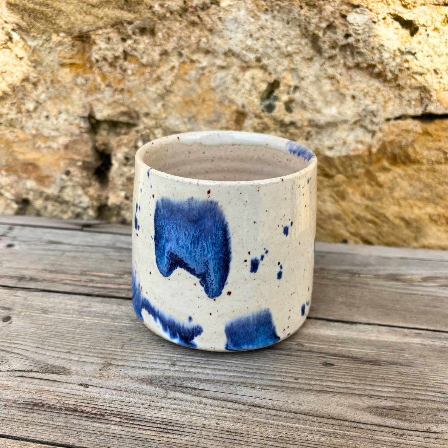 Ceramic cup with blue speckles on a wooden surface with a stone wall background