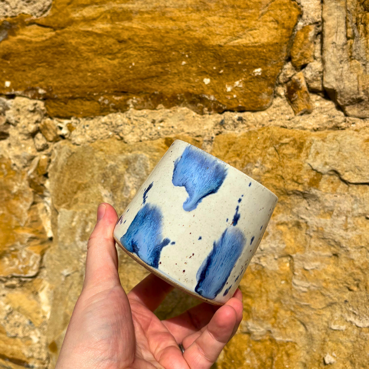 Hand holding a ceramic mug with blue abstract patterns against a stone wall background