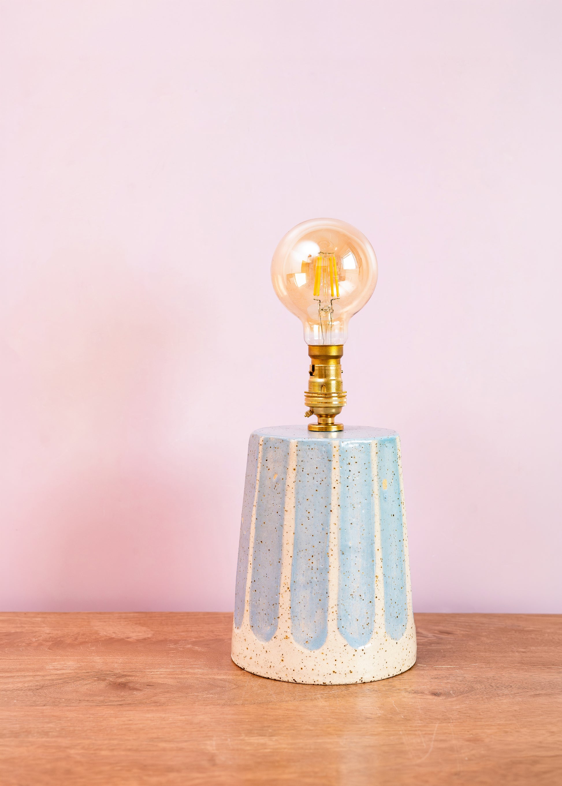 Ceramic lamp with a vintage-style light bulb on a wooden surface and pink background