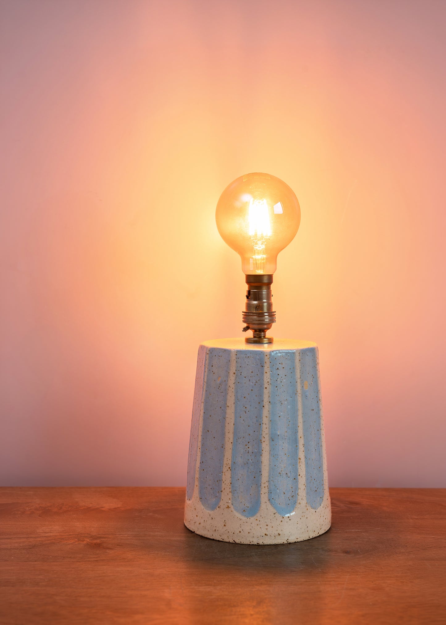 Table lamp with a textured concrete base and lit bulb on a wooden surface.