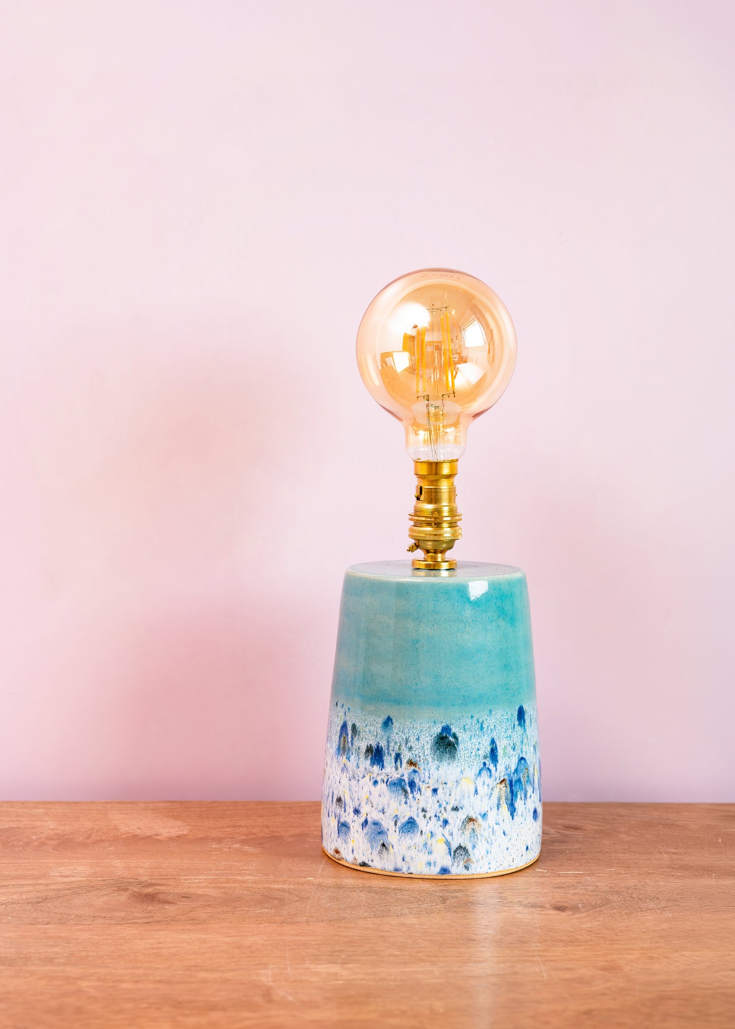 Decorative lamp with a blue and white speckled base and gold bulb on a wooden surface with a pink background