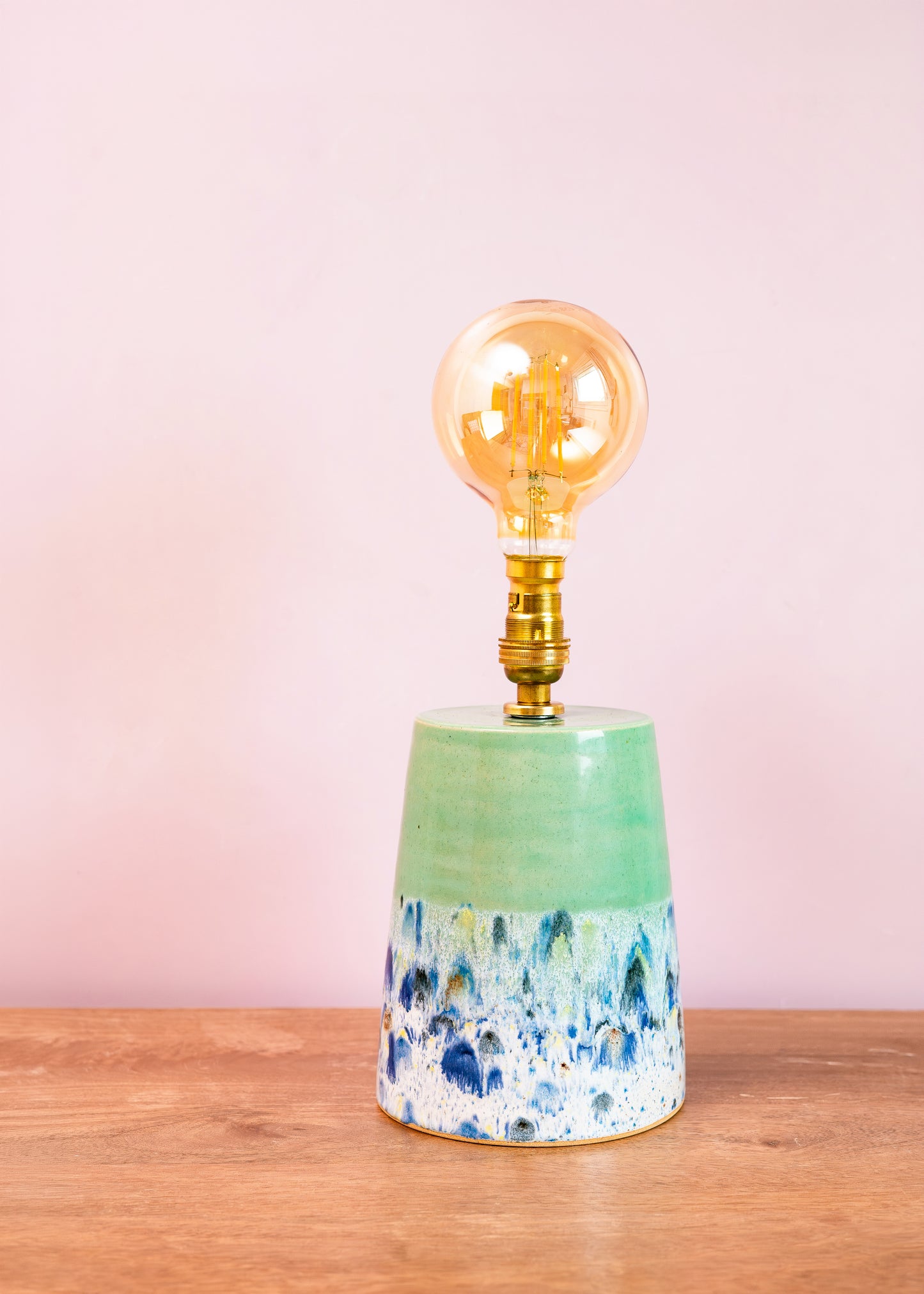Decorative lamp with a ceramic base and gold bulb on a wooden surface with a pink background