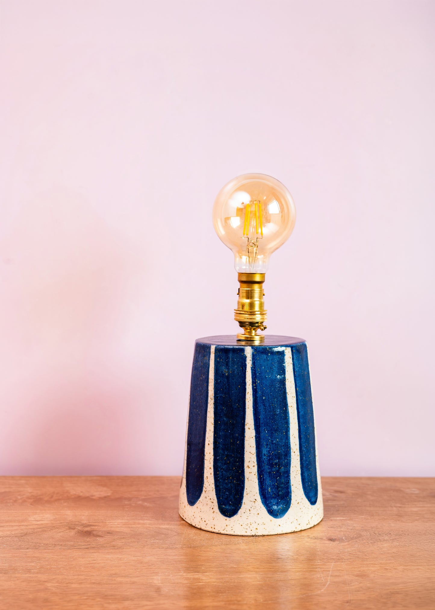 Table lamp with a blue and white striped base and a clear bulb on a wooden surface with a pink background.