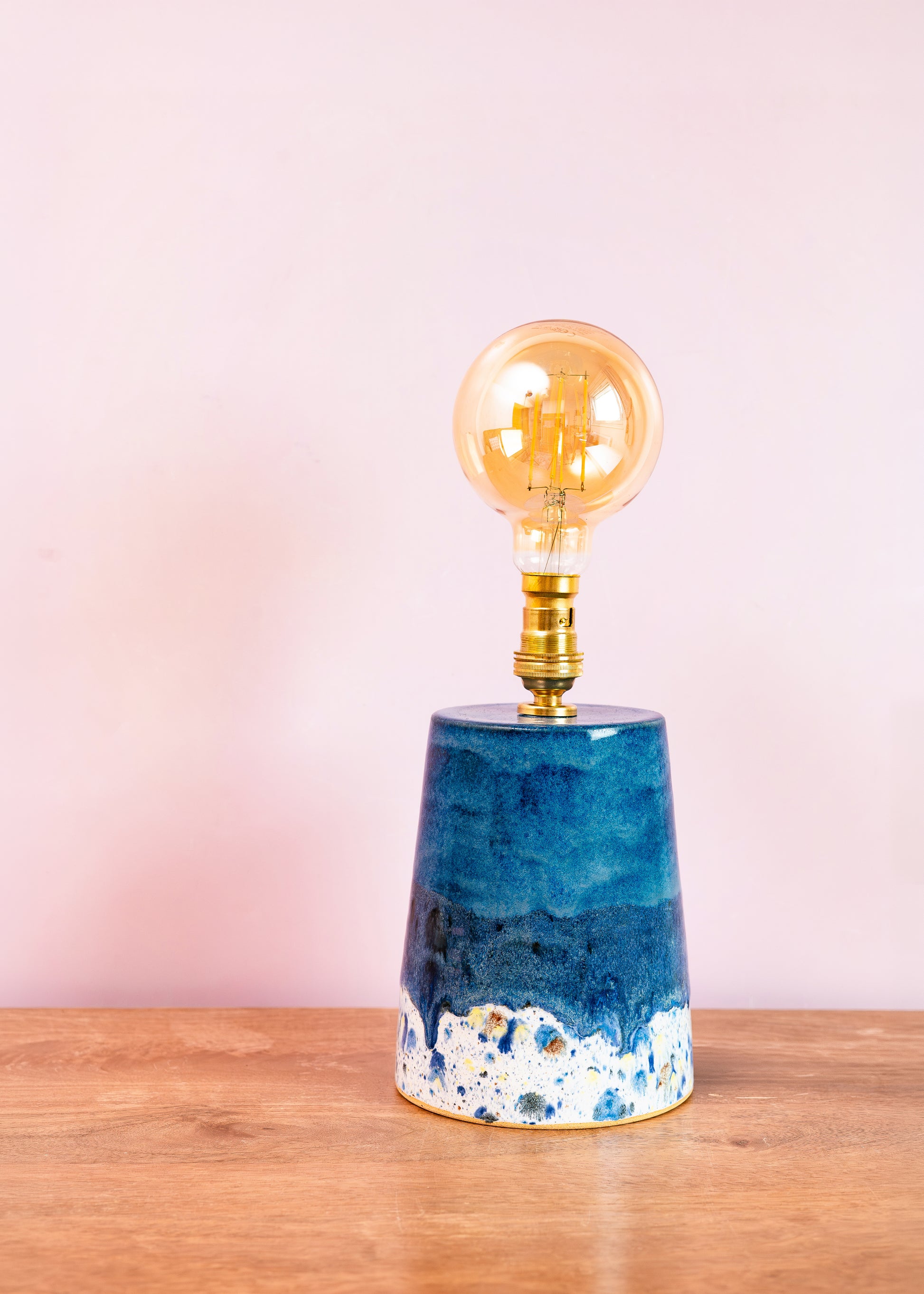 Blue ceramic lamp with a gold bulb on a wooden surface and pink background