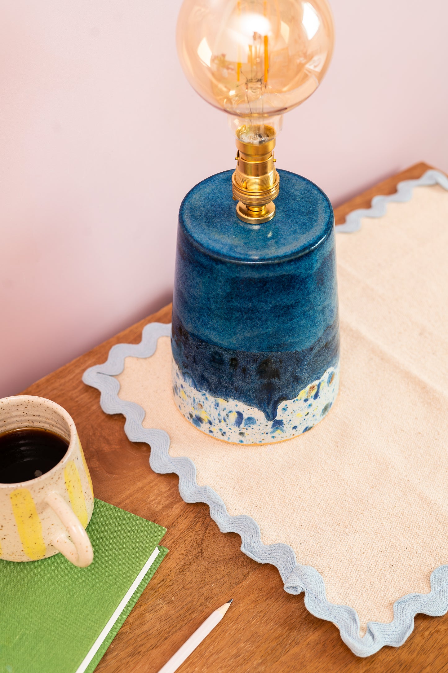 Blue ceramic lamp with a vintage-style light bulb on a wooden table with a mug and notebook.