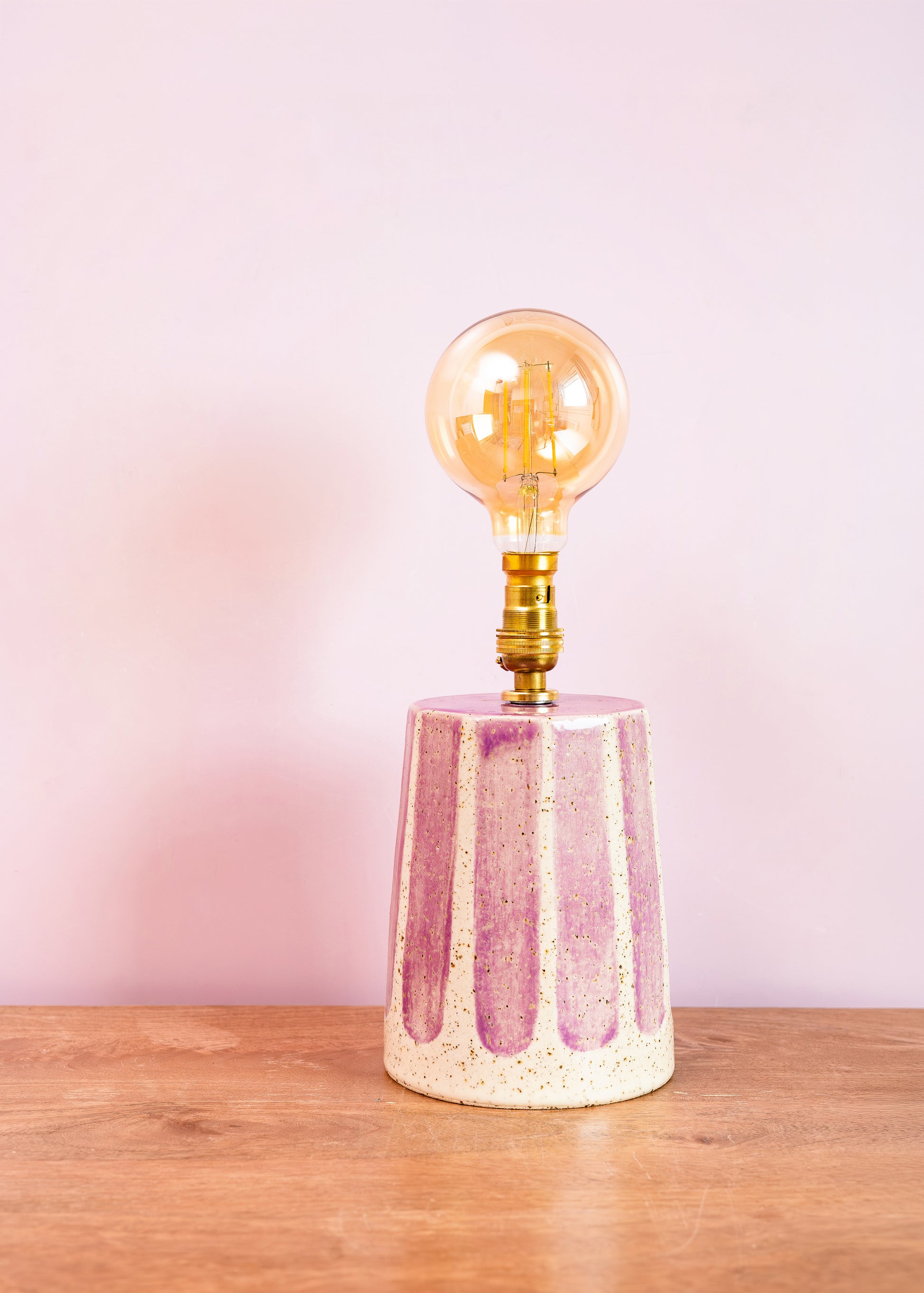 Decorative lamp with a pink ceramic base and gold bulb on a wooden surface with a pink background