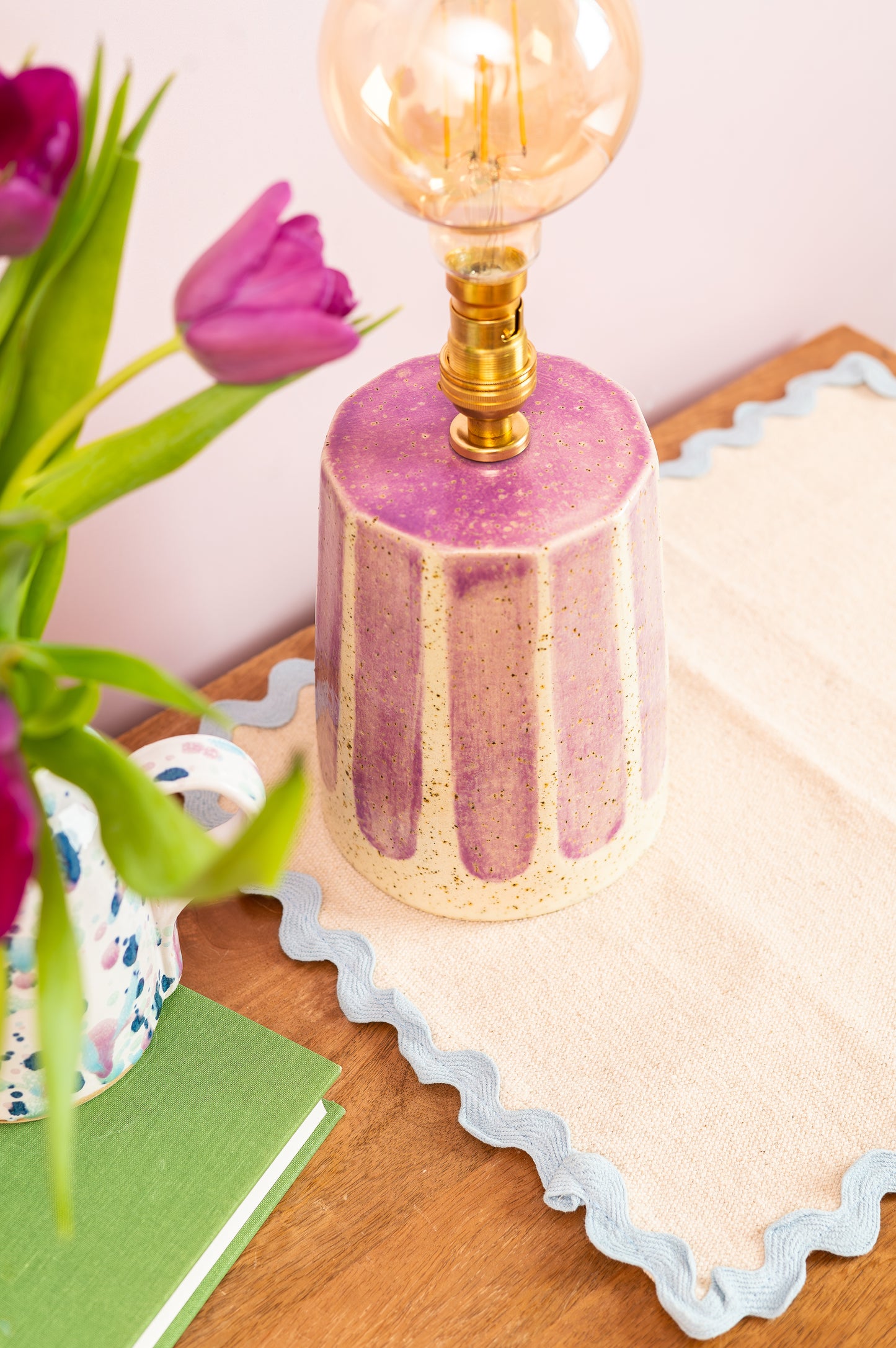 Pink textured lamp with a light bulb on a wooden surface with tulips and a card.