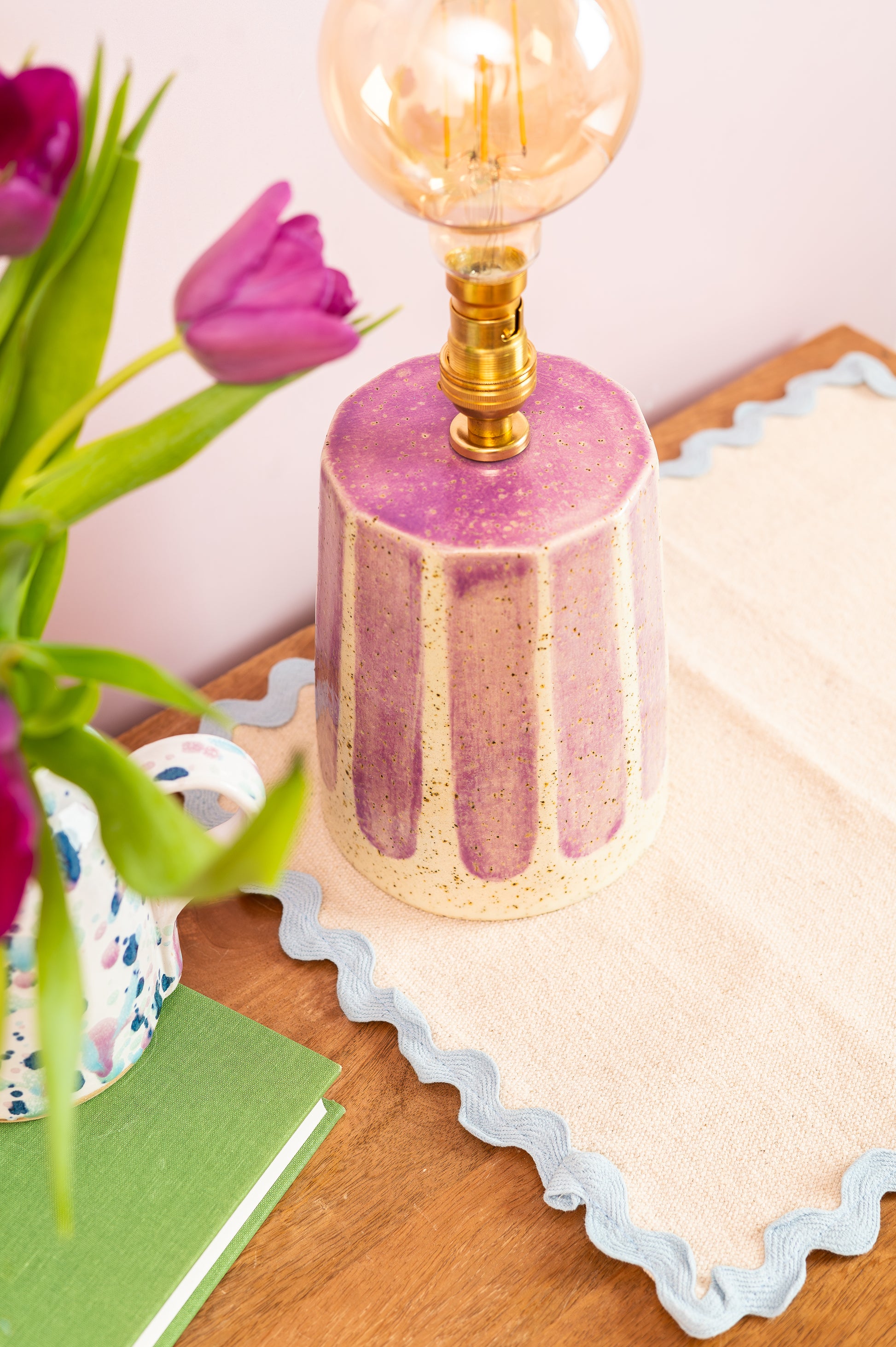 Pink textured lamp with a light bulb on a wooden surface with tulips and a card.