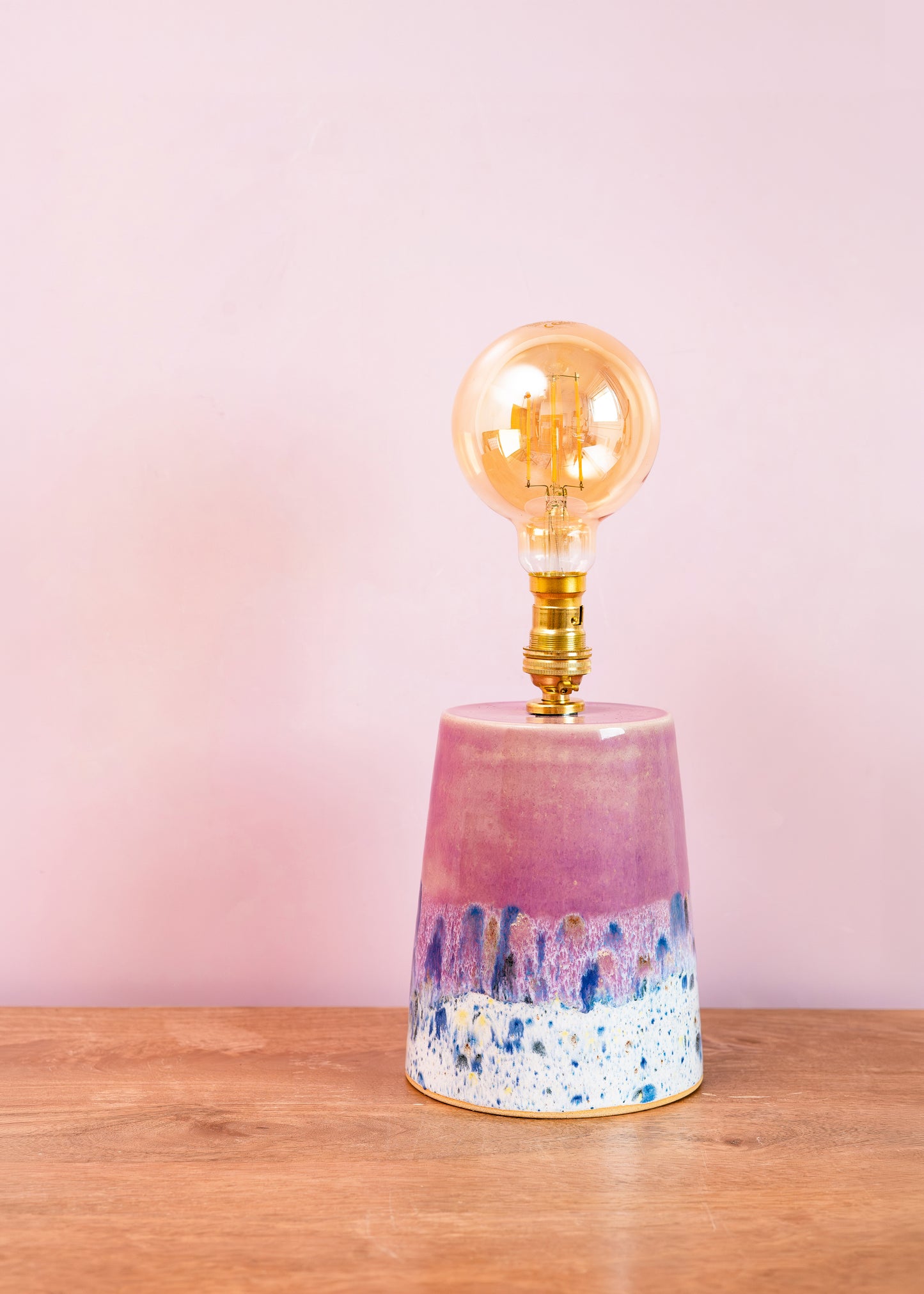 Decorative lamp with a pink and blue base on a wooden surface against a pink background