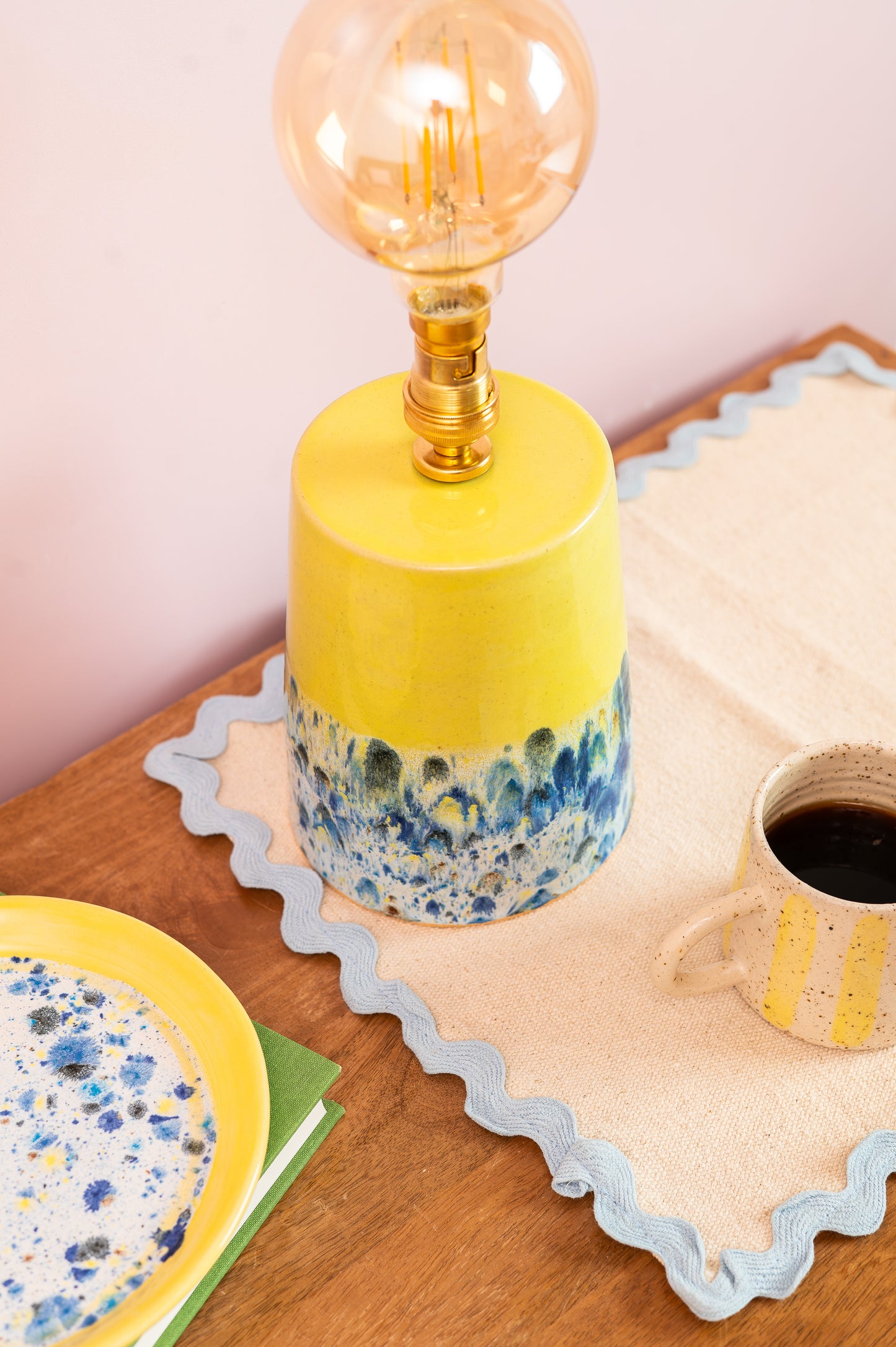 Yellow lamp with blue speckled design on a wooden table with a cup and saucer.