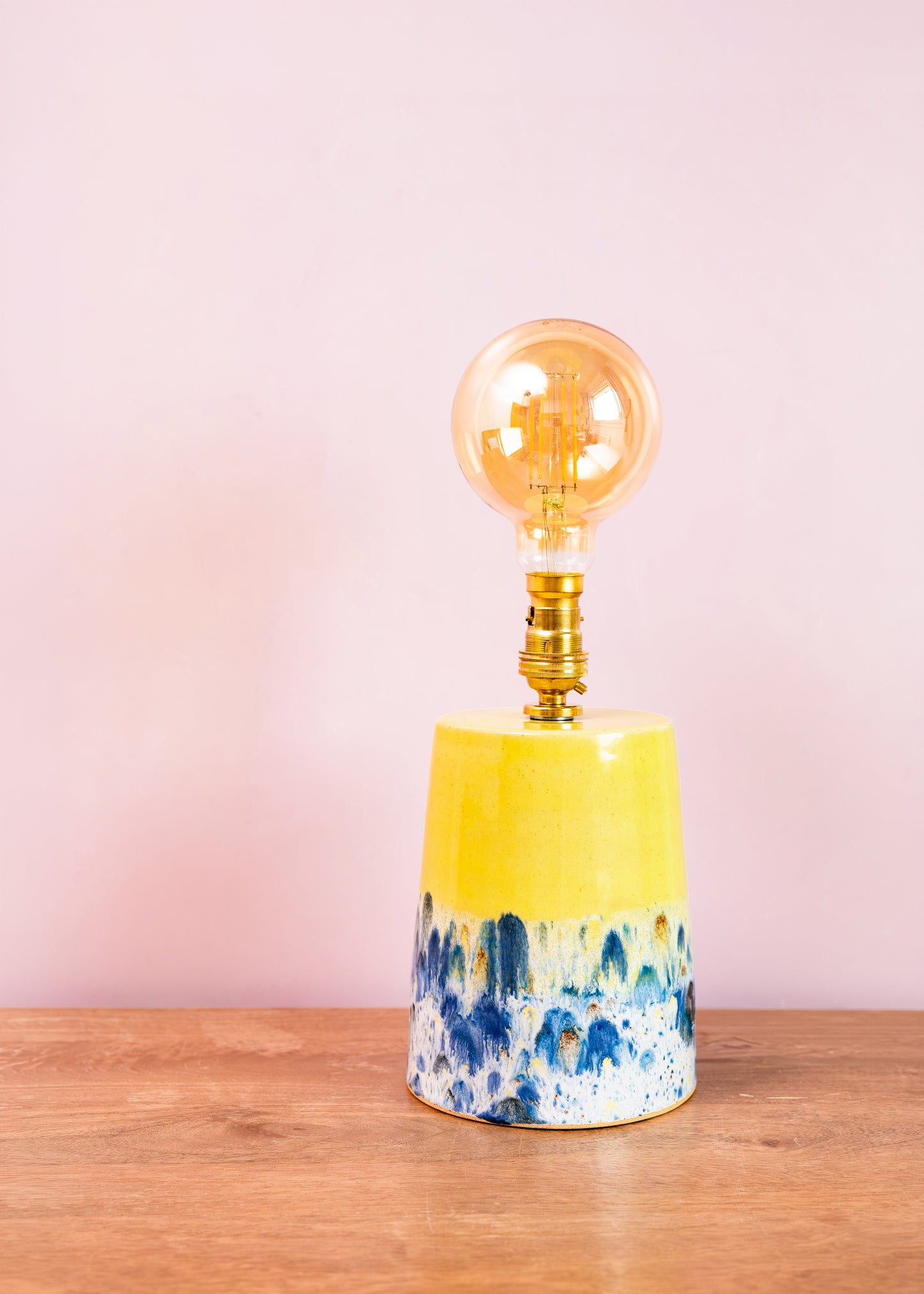 Decorative lamp with a yellow base and blue abstract design on a wooden surface with a pink background