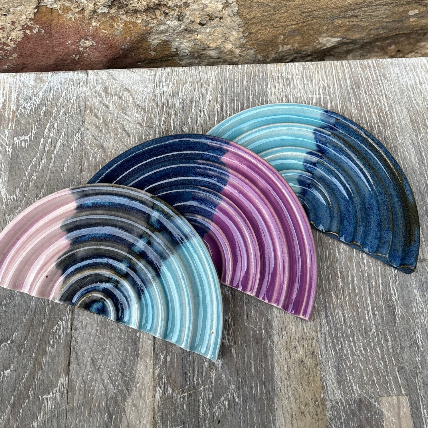 Three curved ceramic soap dishes with blue and pink concentric patterns on a wooden surface.