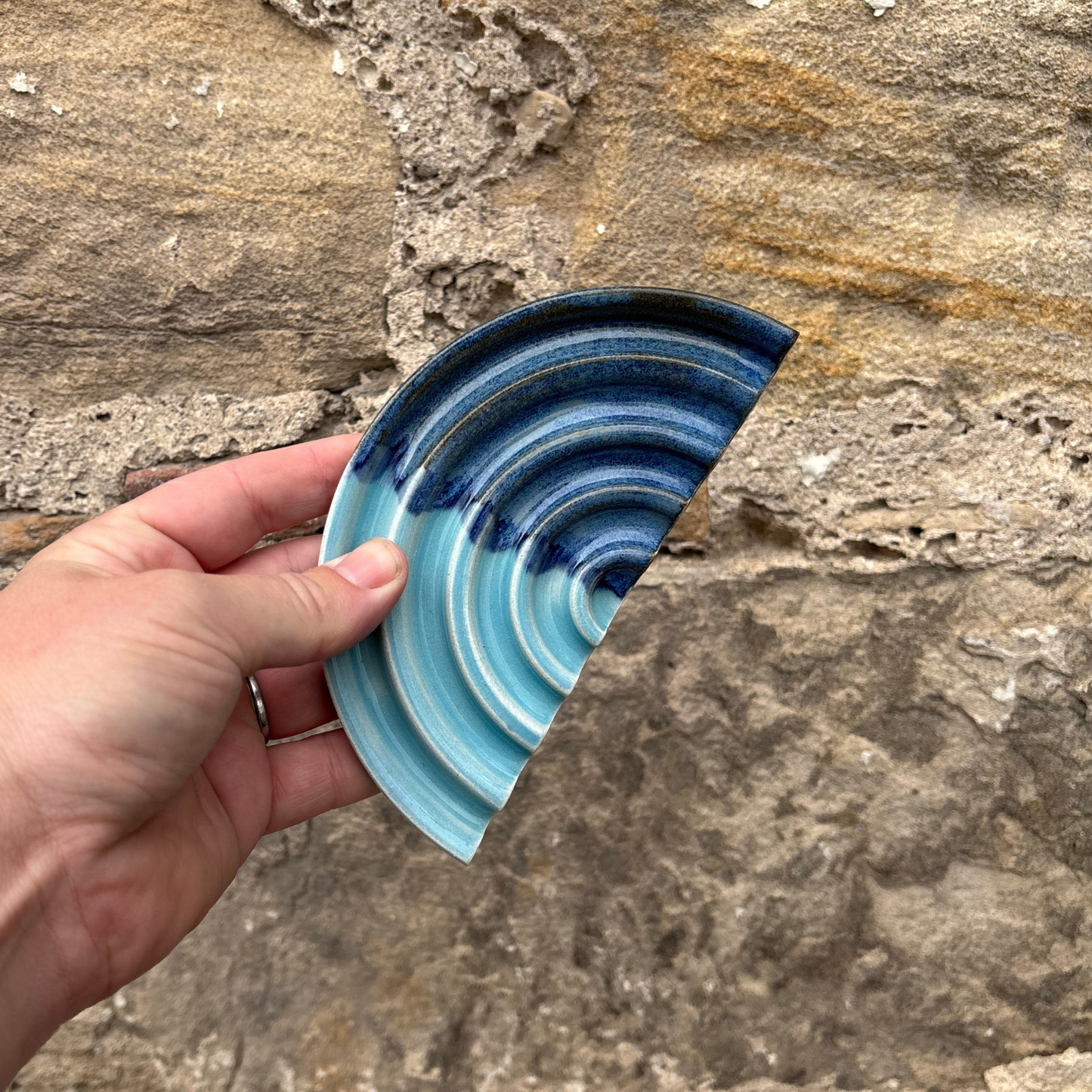 Hand holding a blue ceramic dish against a stone background