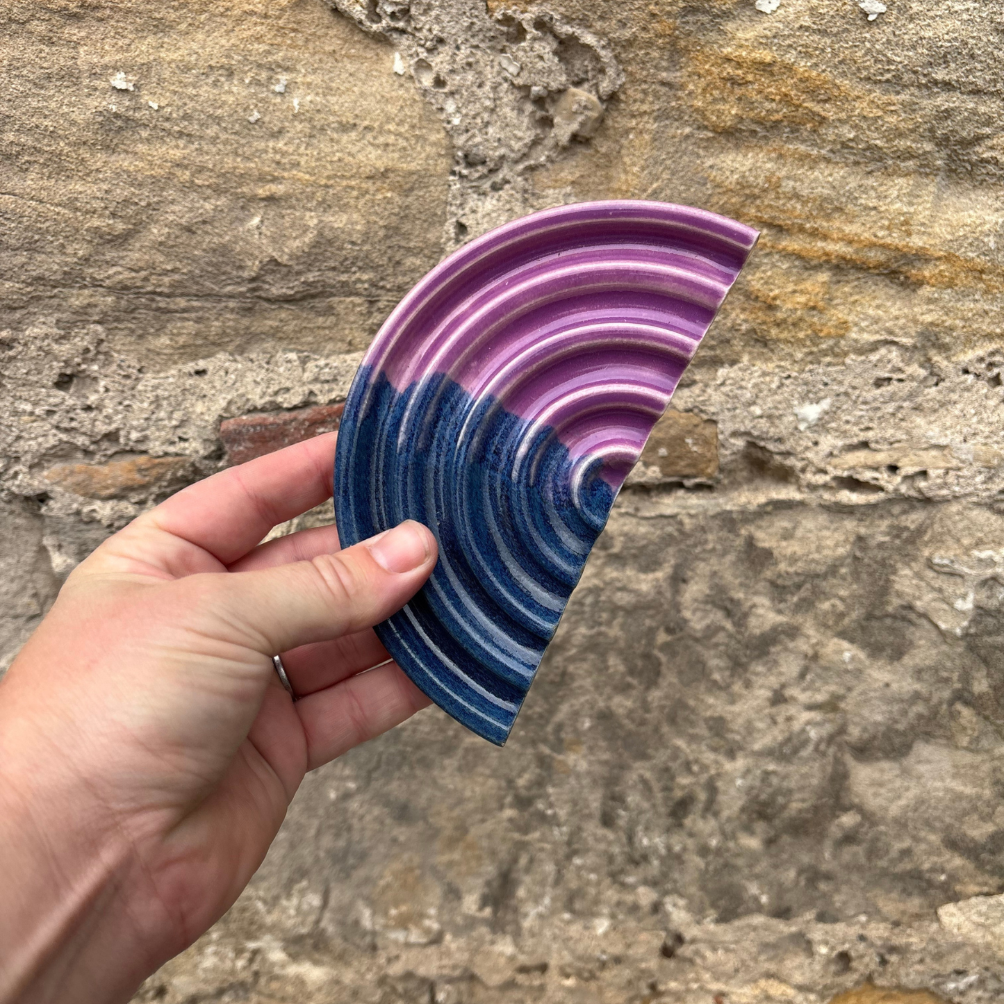 Hand holding a colorful, wavy-patterned soap dish against a stone background