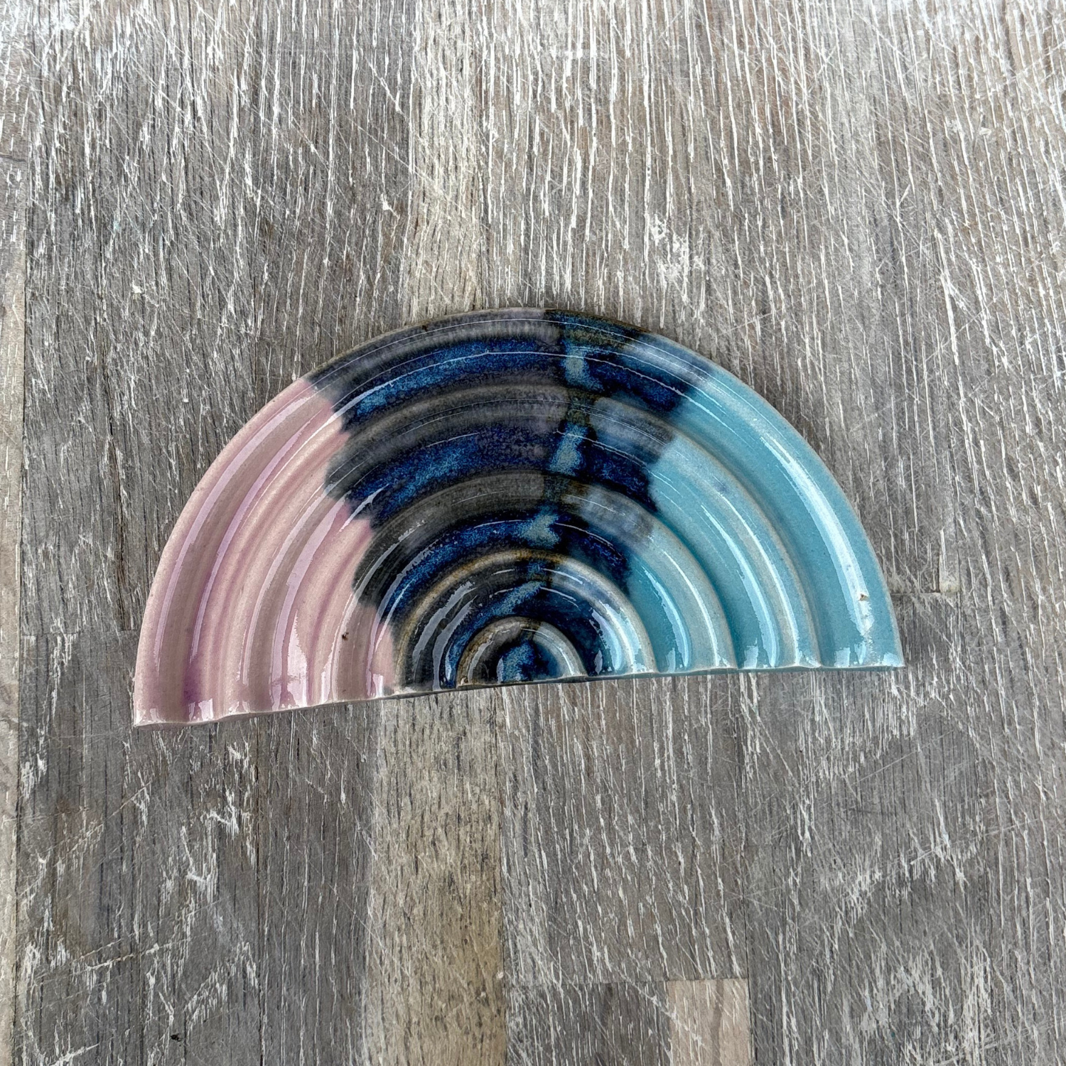 Semicircular ceramic piece with multicolored stripes on a wooden surface